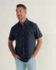 Man standing on white background wearing a navy short sleeve button down and jeans