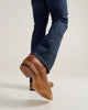 Brown leather shoes worn with blue jeans on a plain background