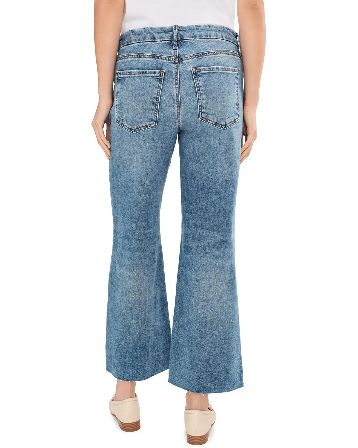 Rear view of a person wearing light blue wide-leg denim jeans with a white top and beige flat shoes, shown against a plain white studio background.
