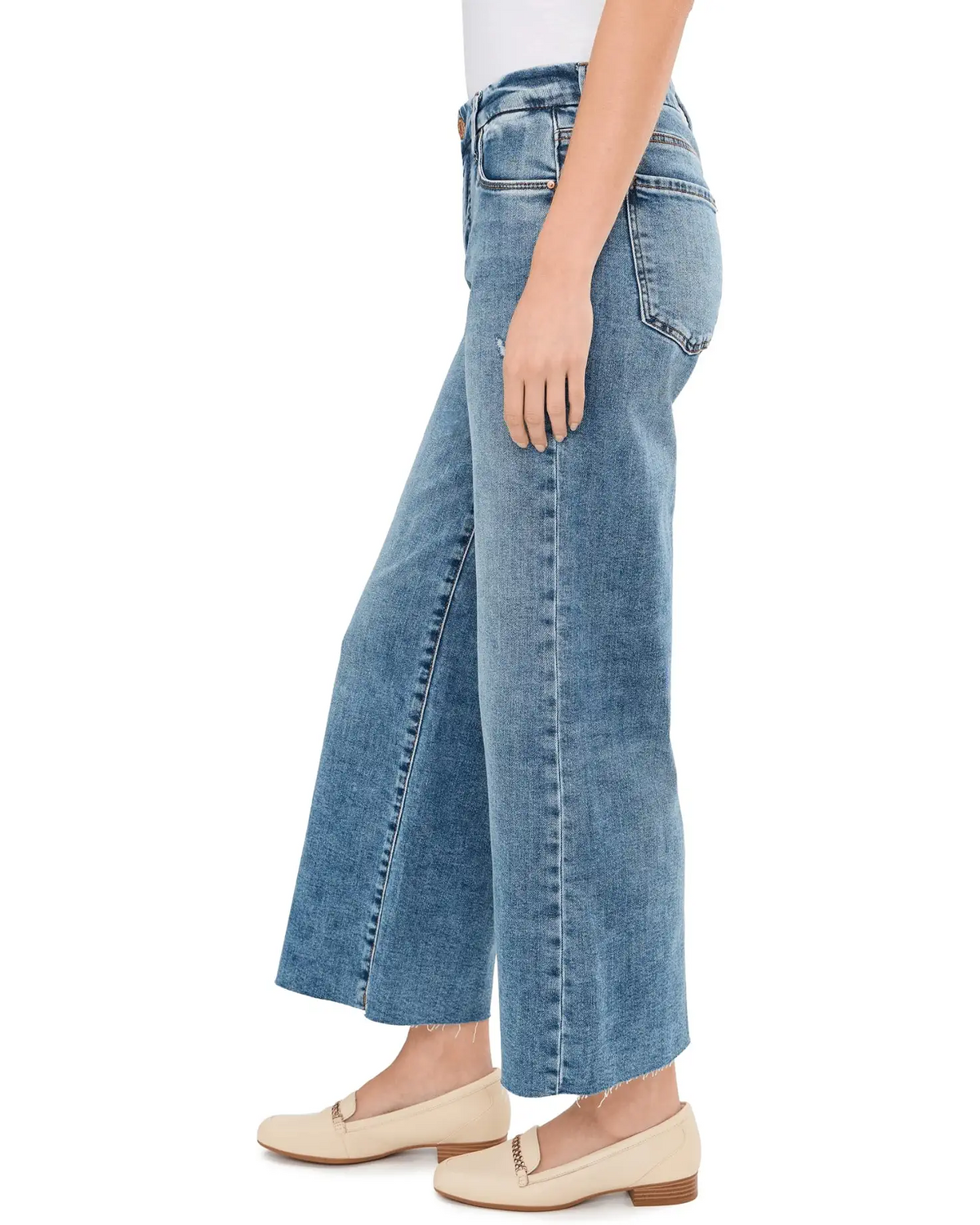 A side profile view of a person wearing light blue wide-leg cropped jeans with beige flat loafers, shown against a plain white background.