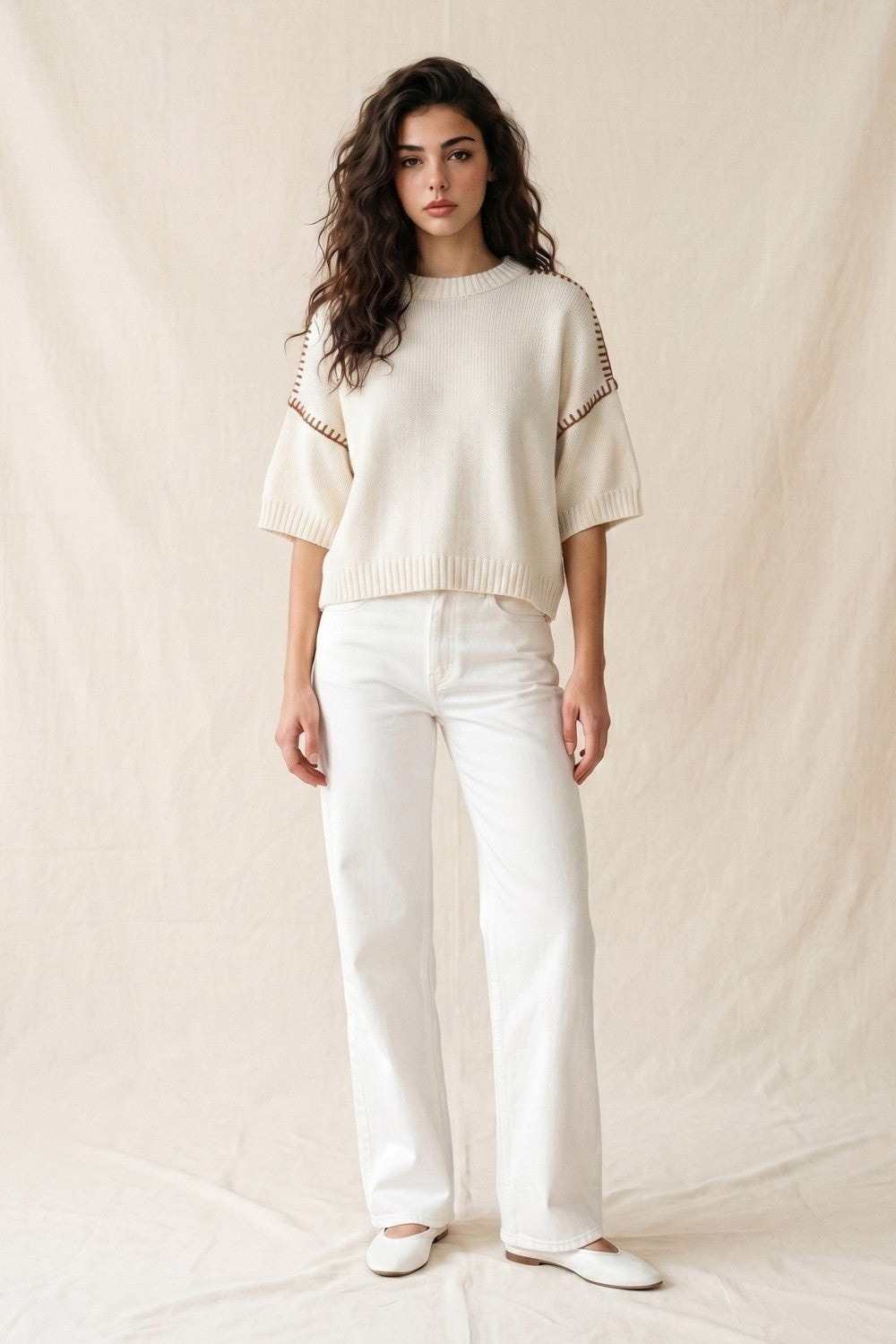 Woman wearing a white sweater and pants against a plain background