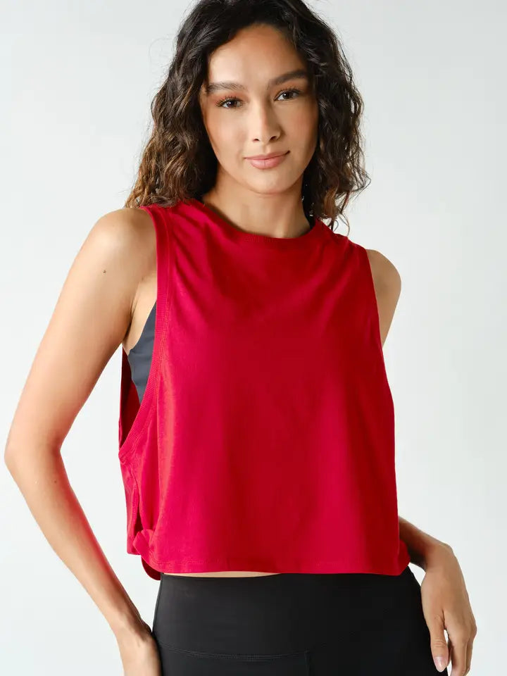 A woman modeling a sleeveless crop top in a vibrant red color, paired with black pants, against a plain light gray studio background.
