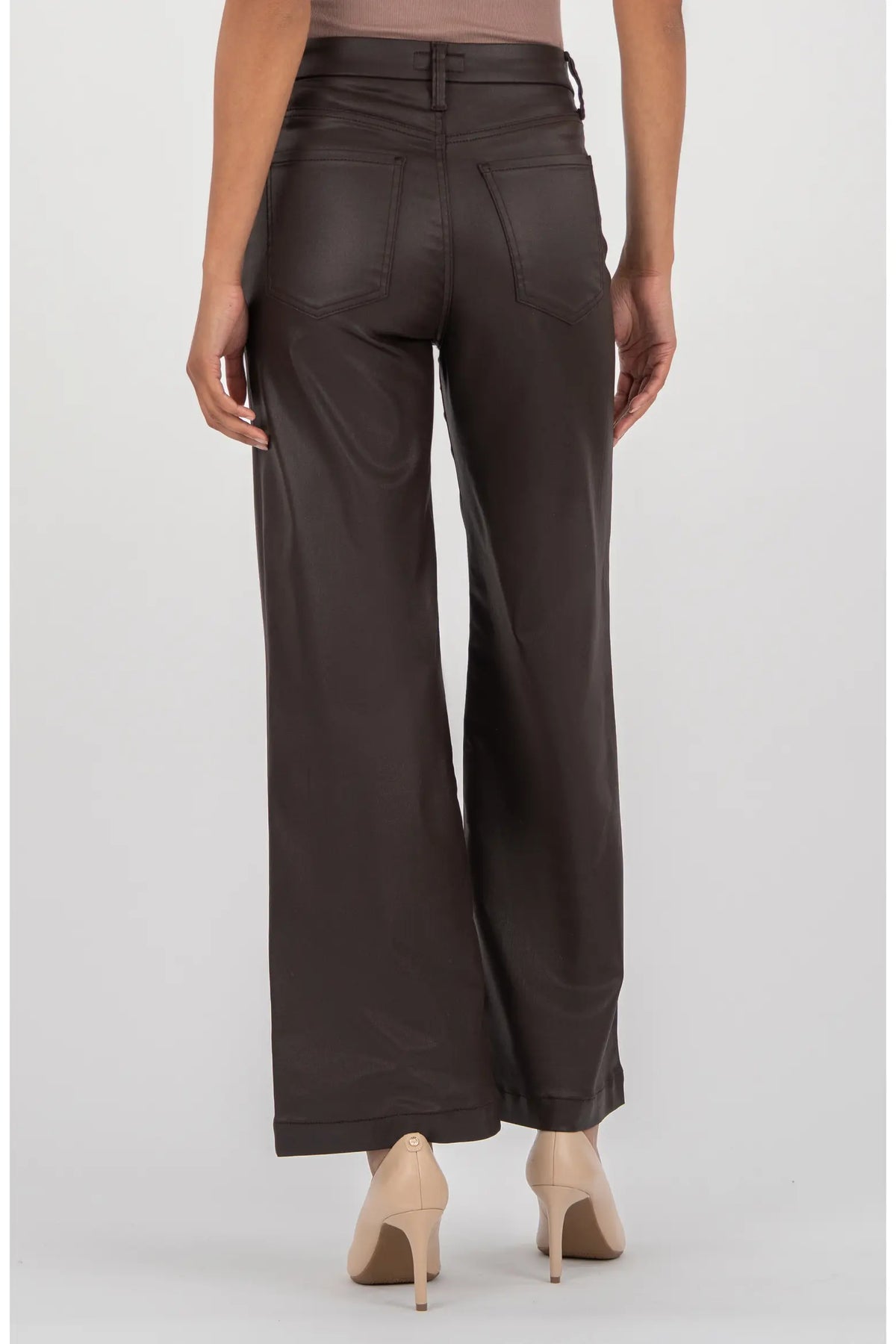 A person shown from the back wearing dark brown wide-leg pants with a faux-leather finish, paired with beige high heels against a light gray studio background.