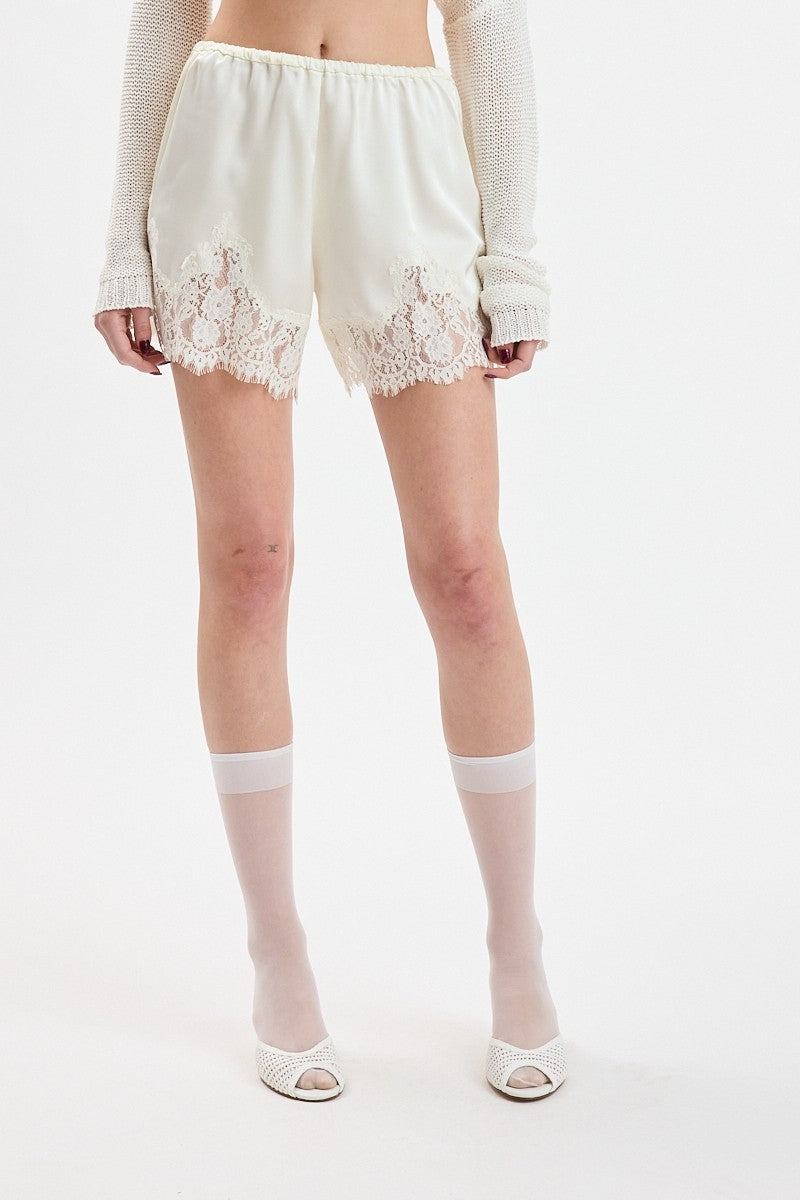 Person wearing white lace shorts and sheer socks on a plain background