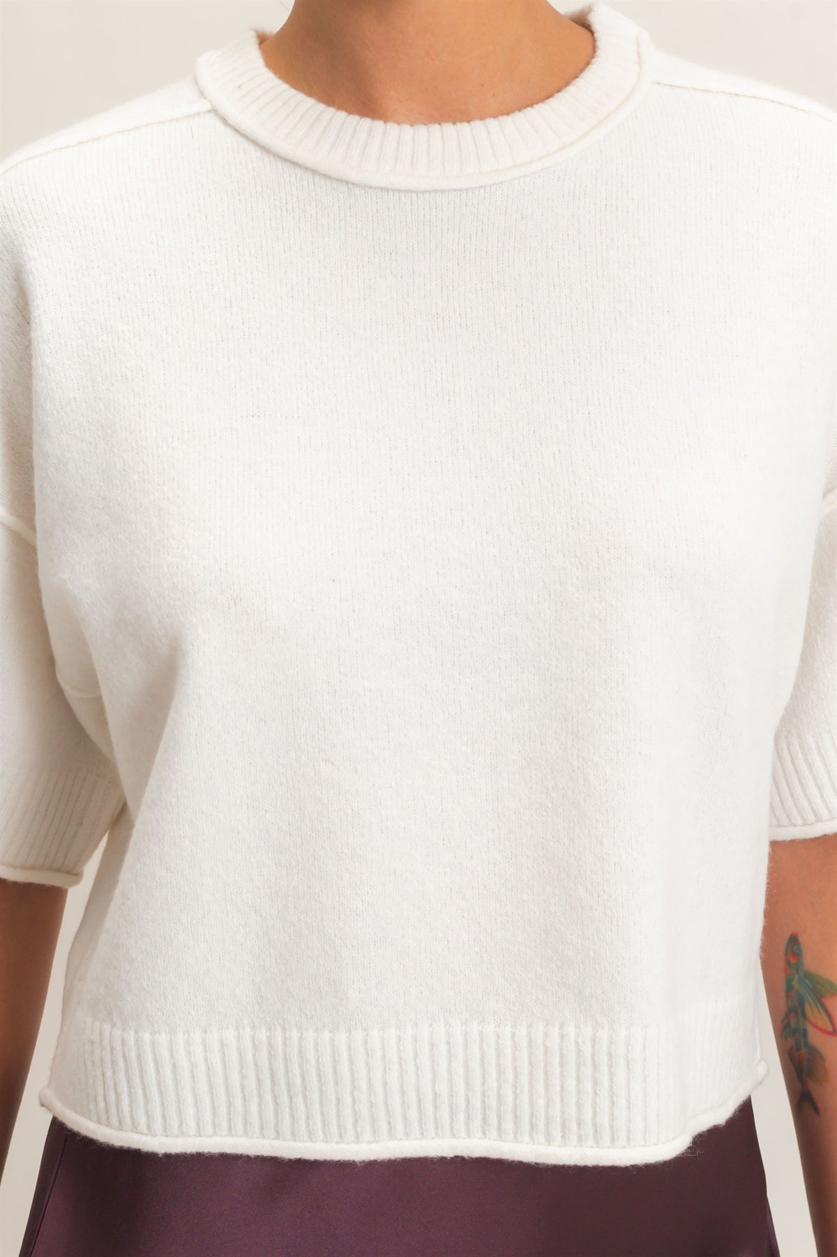 White knit sleeveless top worn by a person with a tattoo on their arm.