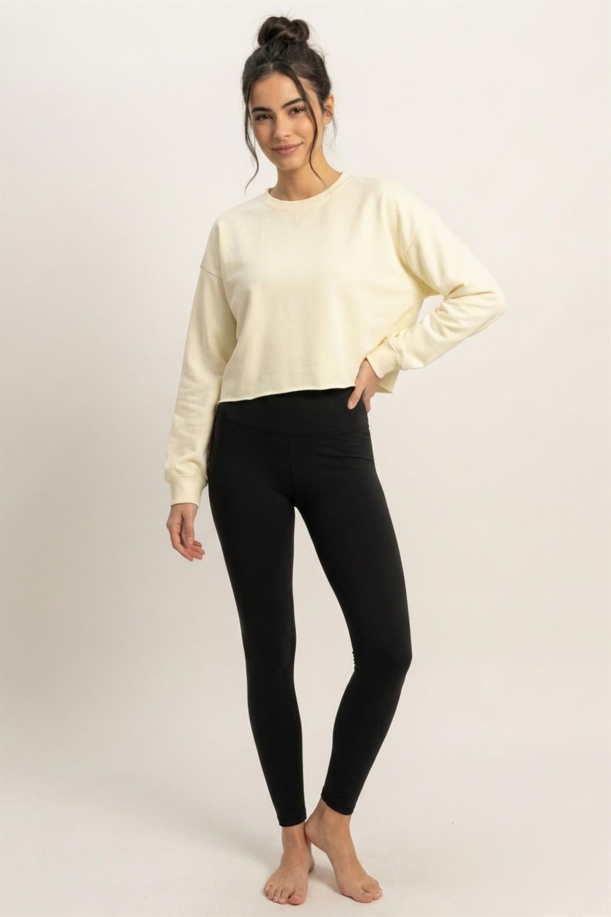 Woman wearing a cream sweater and black leggings on a plain background