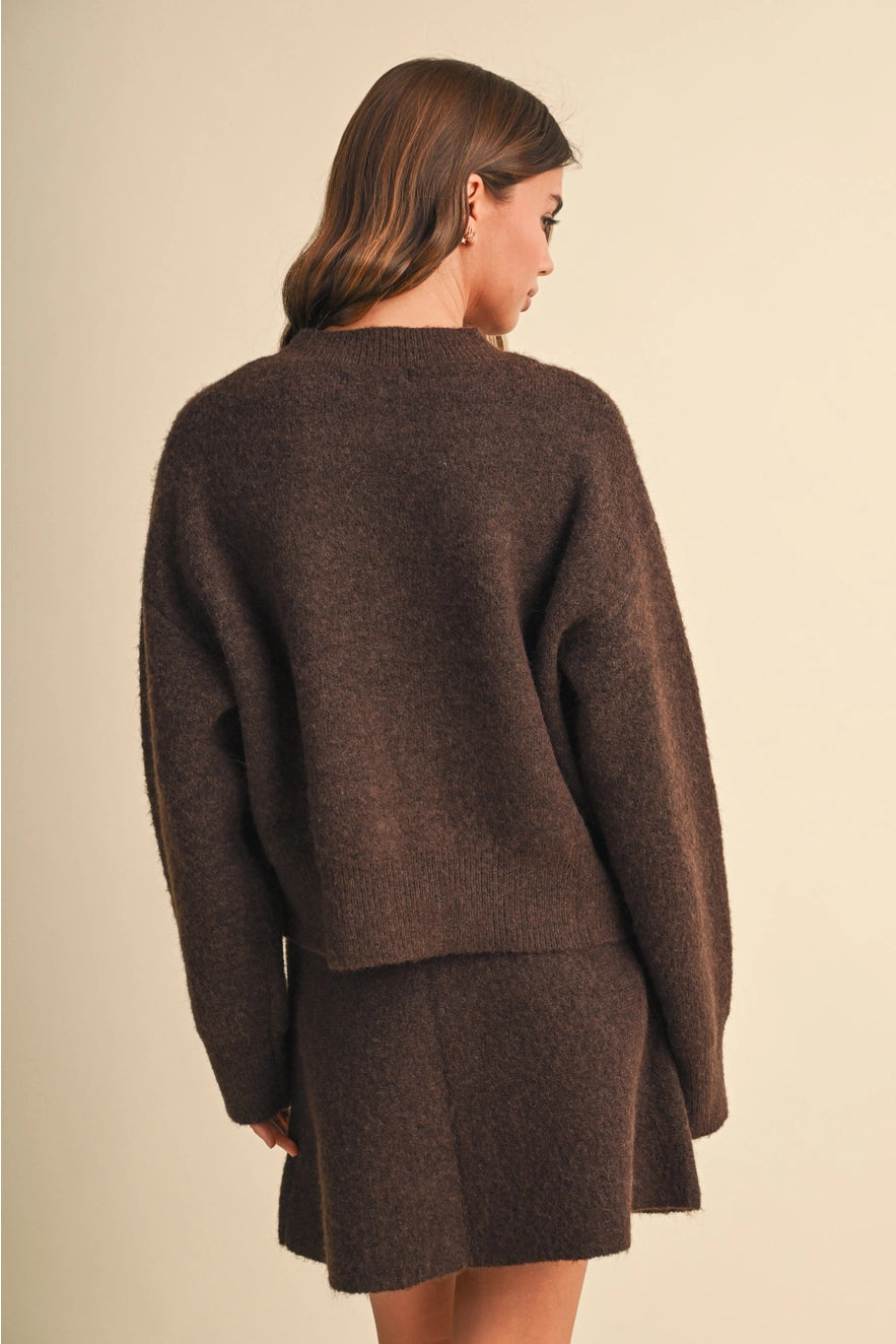 A woman shown from the back wearing a dark brown fuzzy knit sweater and matching skirt against a plain beige studio background.