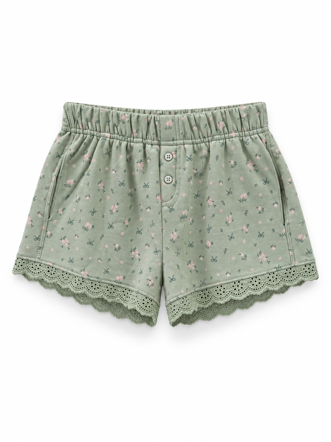 Sage green shorts with a pink floral and dark green bow print, elastic waistband, two front buttons, side pockets, and scalloped lace hems on a white background.