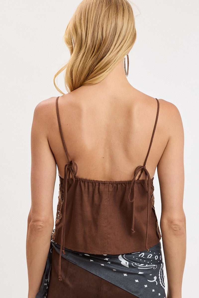 Rear view of a woman wearing a brown spaghetti-strap camisole top with side tie details, paired with a dark patterned skirt, against a plain white background.