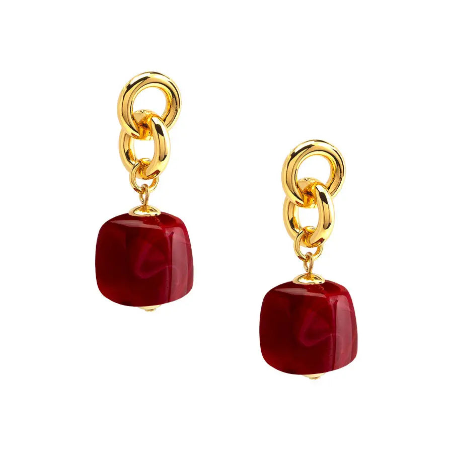 A pair of gold-tone drop earrings featuring a polished, rounded square red gemstone dangle, shown against a plain white background.