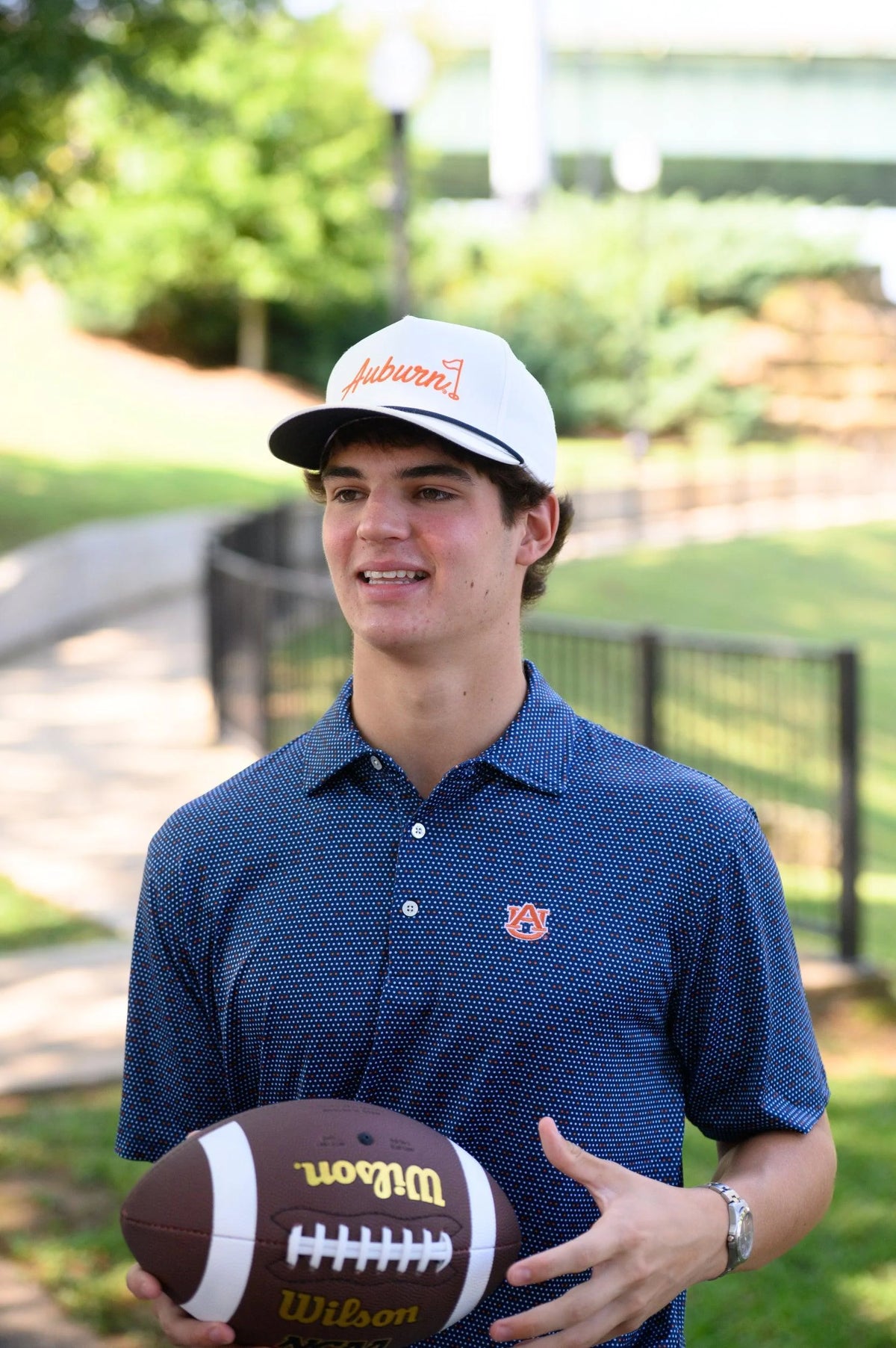 Person wearing an Auburn cap and holding a football outdoors