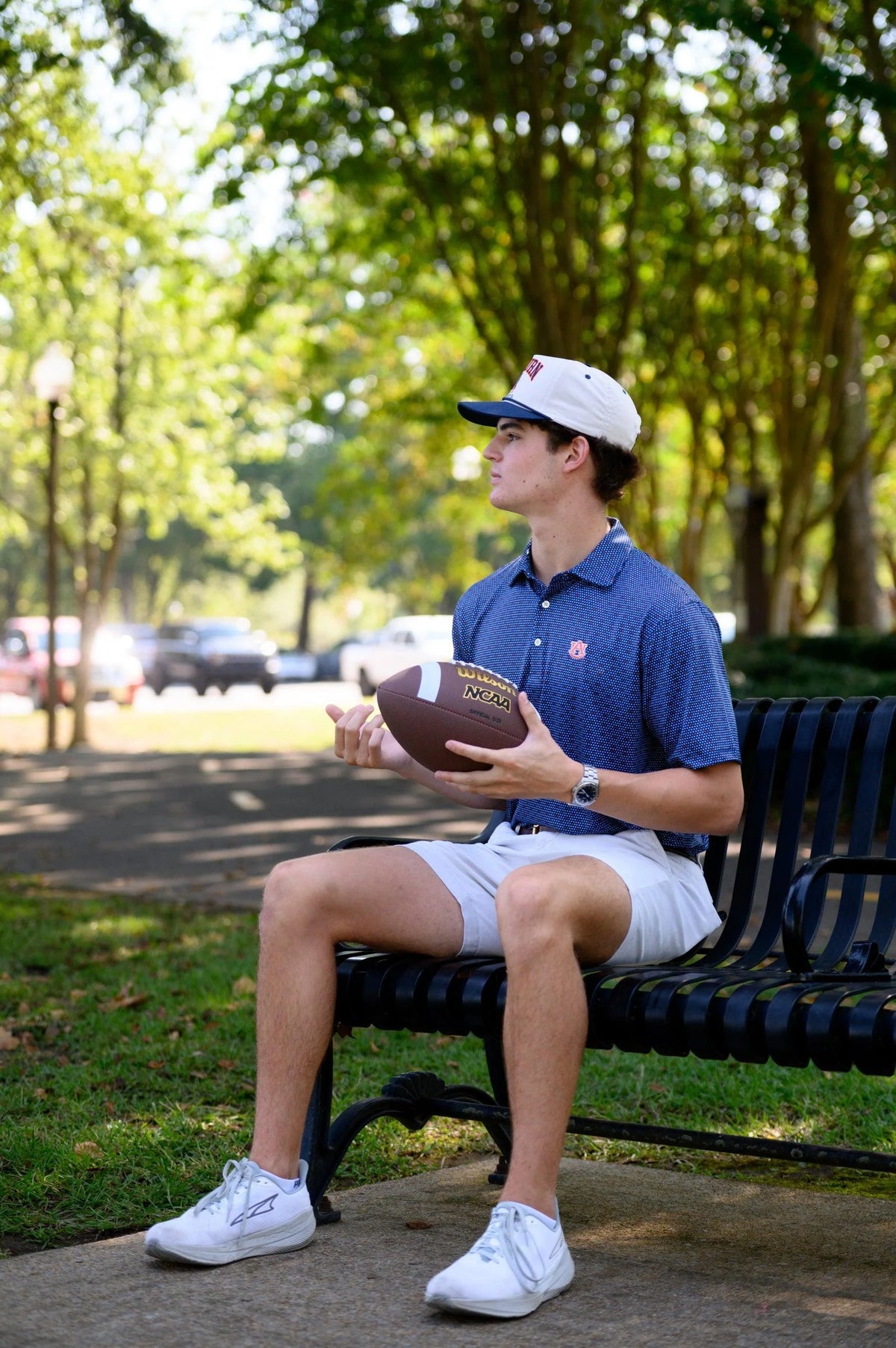 Person sitting on a bench holding a football in a park-like setting