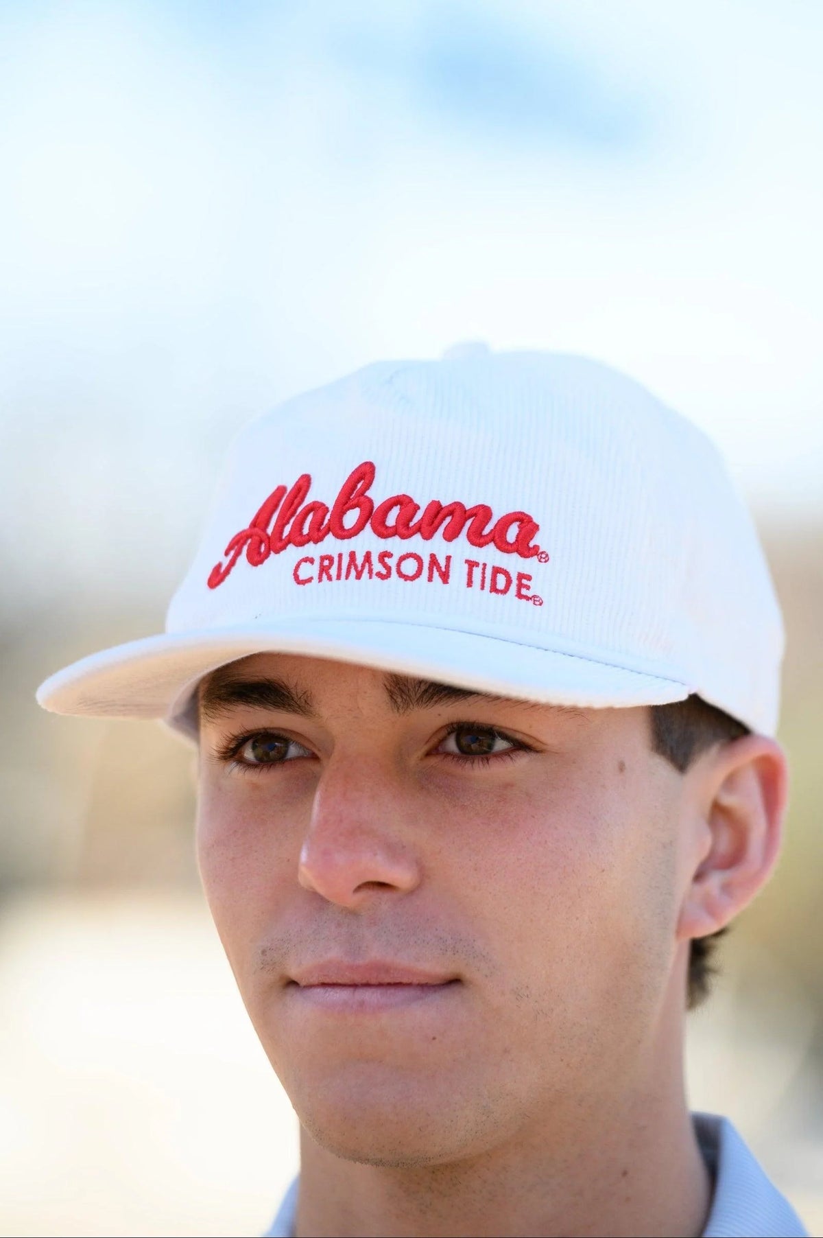 Person wearing a white cap with 'Alabama Crimson Tide' text against a blurred background