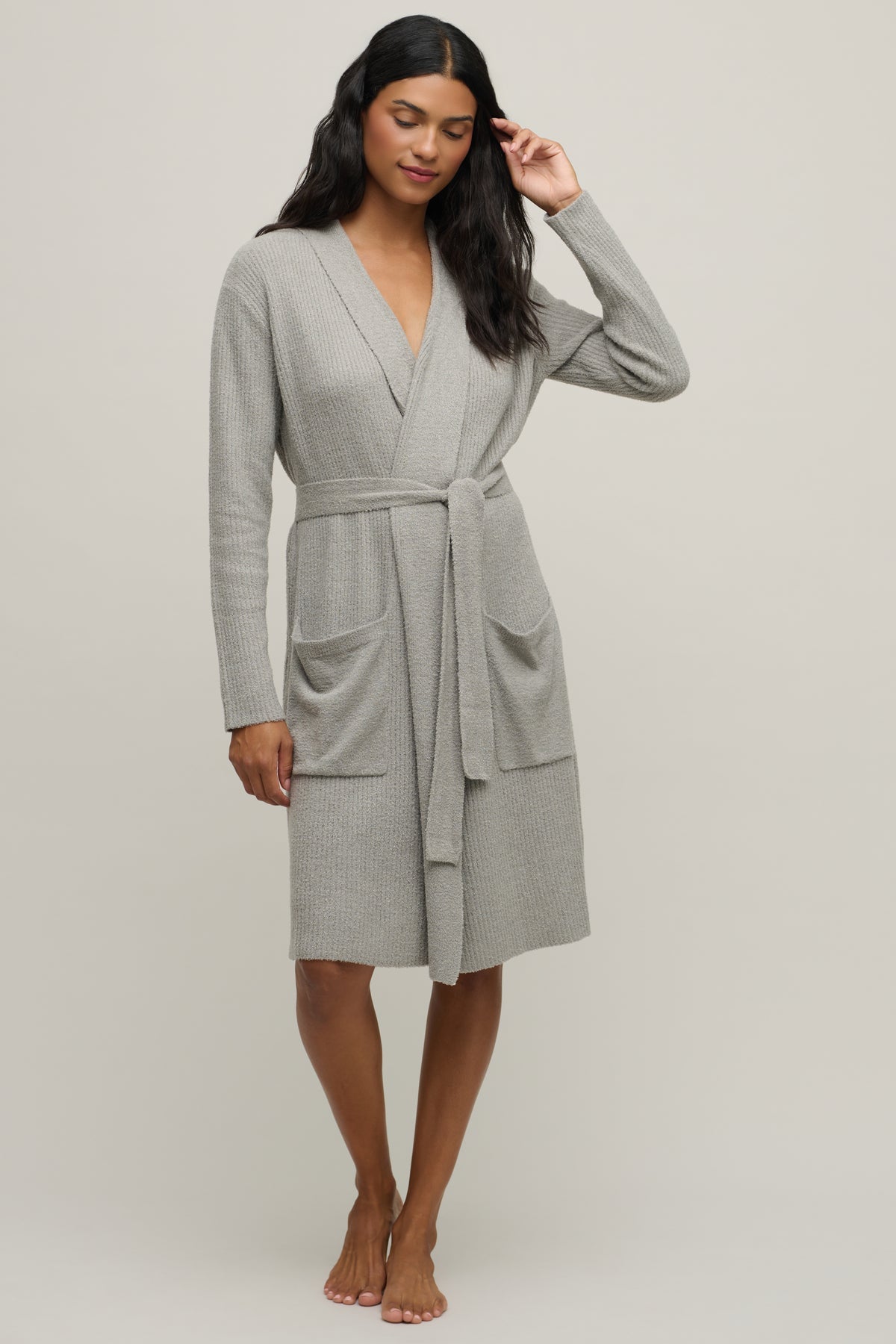 A woman modeling a light gray long-sleeve bathrobe with a tie waist and front patch pockets, photographed against a plain light gray studio background.