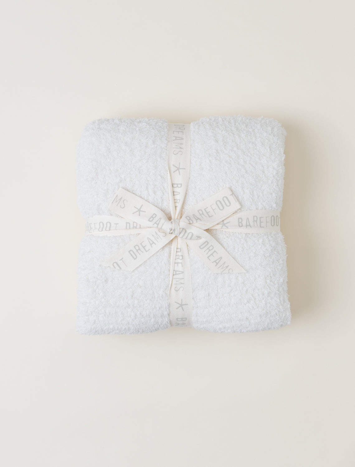 Folded textured blanket with a brand label on a light beige background