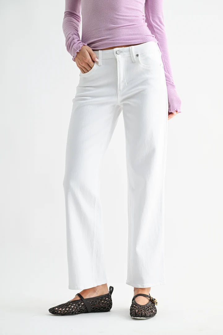 A model wearing white wide-leg cropped jeans, a light purple long-sleeve top, and black woven flats, shown from the waist down against a plain white studio background.