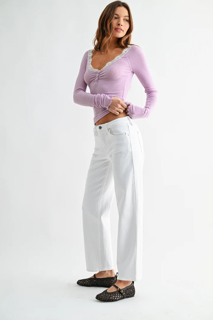 A woman modeling a light purple long-sleeve top with a lace-trimmed scoop neck and white wide-leg jeans, paired with black studded flats, against a plain white studio background.