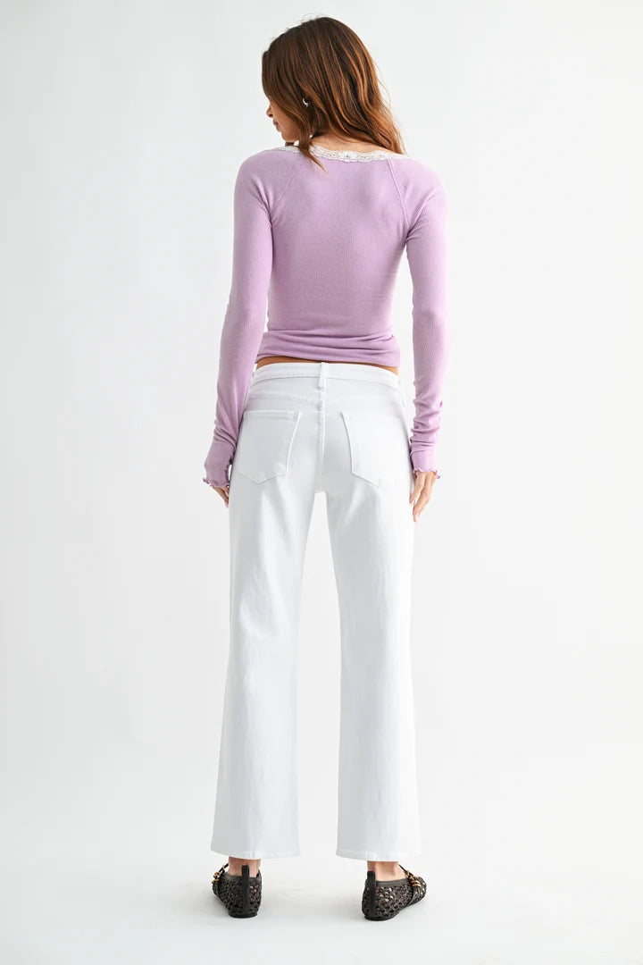 A woman shown from the back wearing a lavender long-sleeve top, white wide-leg cropped pants, and black lace-up flats against a plain white studio background.