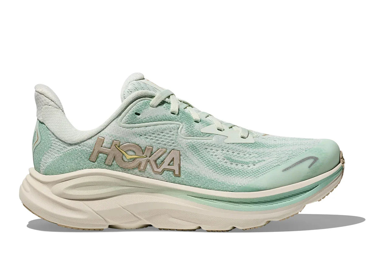 A Hoka running shoe in mint green and cream, featuring a textured mesh upper, a thick cushioned sole, and a metallic gold Hoka logo on the side, set against a plain white background.