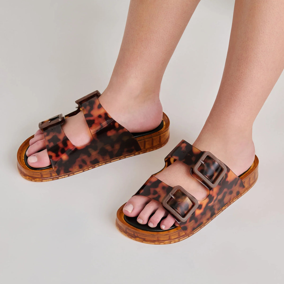 Leopard print sandals with buckles worn by a person on a light background