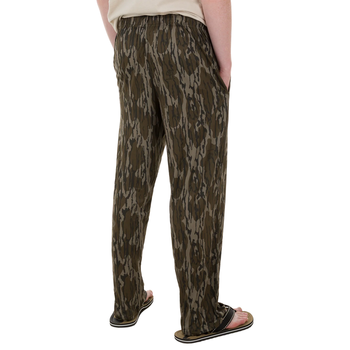 A person shown from the back wearing loose camouflage-print pants and black slide sandals against a plain white studio background.