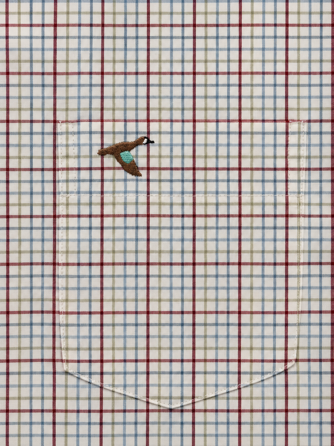 A close-up of a plaid fabric surface with red, blue, and white intersecting lines on a light background, featuring a small embroidered bird motif near the upper left area.