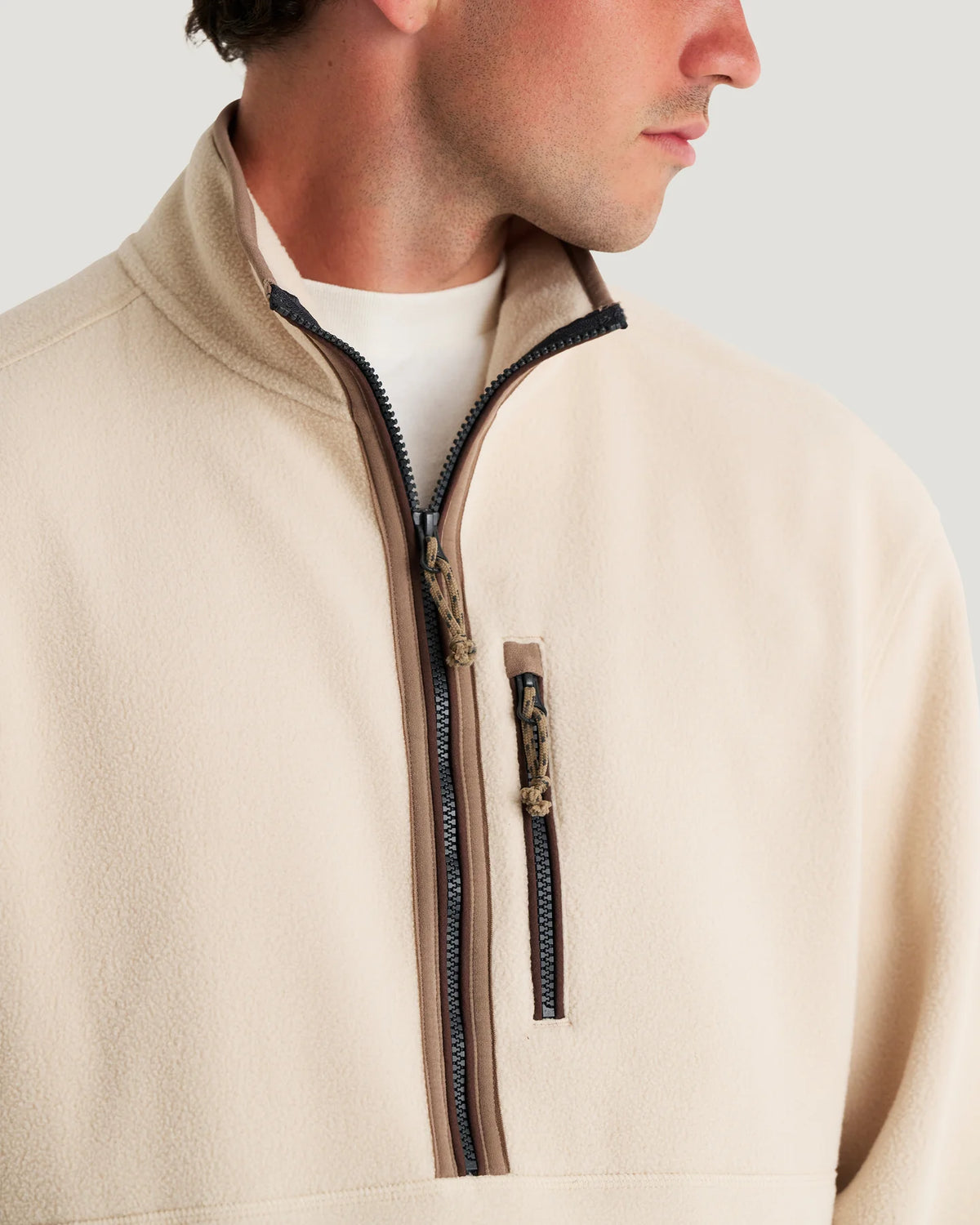 Close-up of a man wearing a light beige fleece quarter-zip pullover with dark zipper trim and a small vertical zip pocket on the chest.