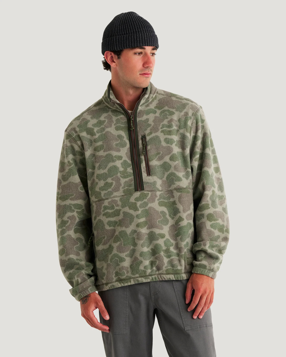 Man wearing a camouflage pullover and black beanie on a light gray background
