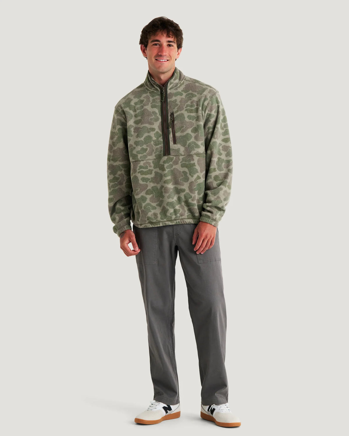 Man wearing a camouflage pullover and gray pants on a white background