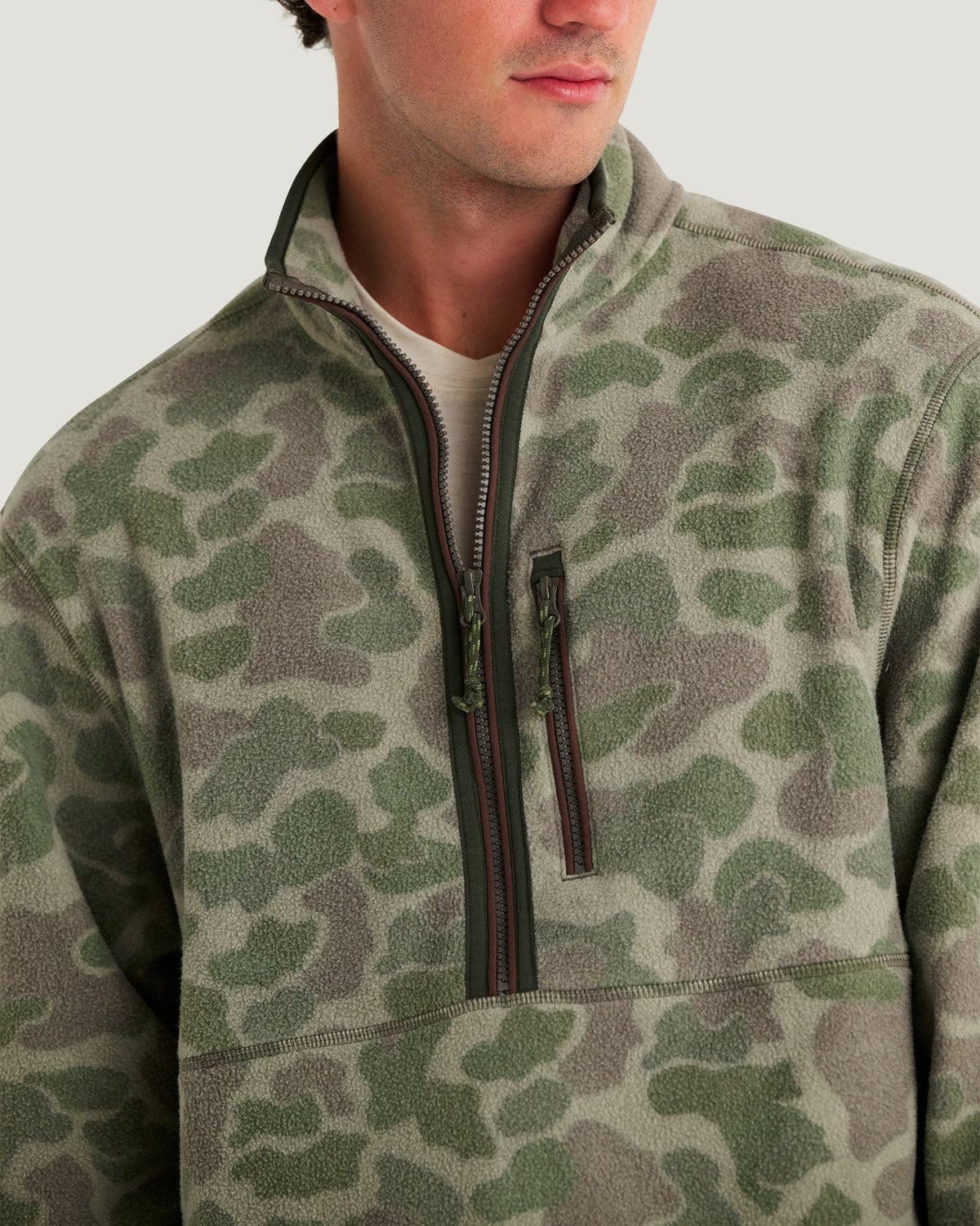 A close-up of a man wearing a fleece quarter-zip pullover in an olive green and gray camouflage pattern.