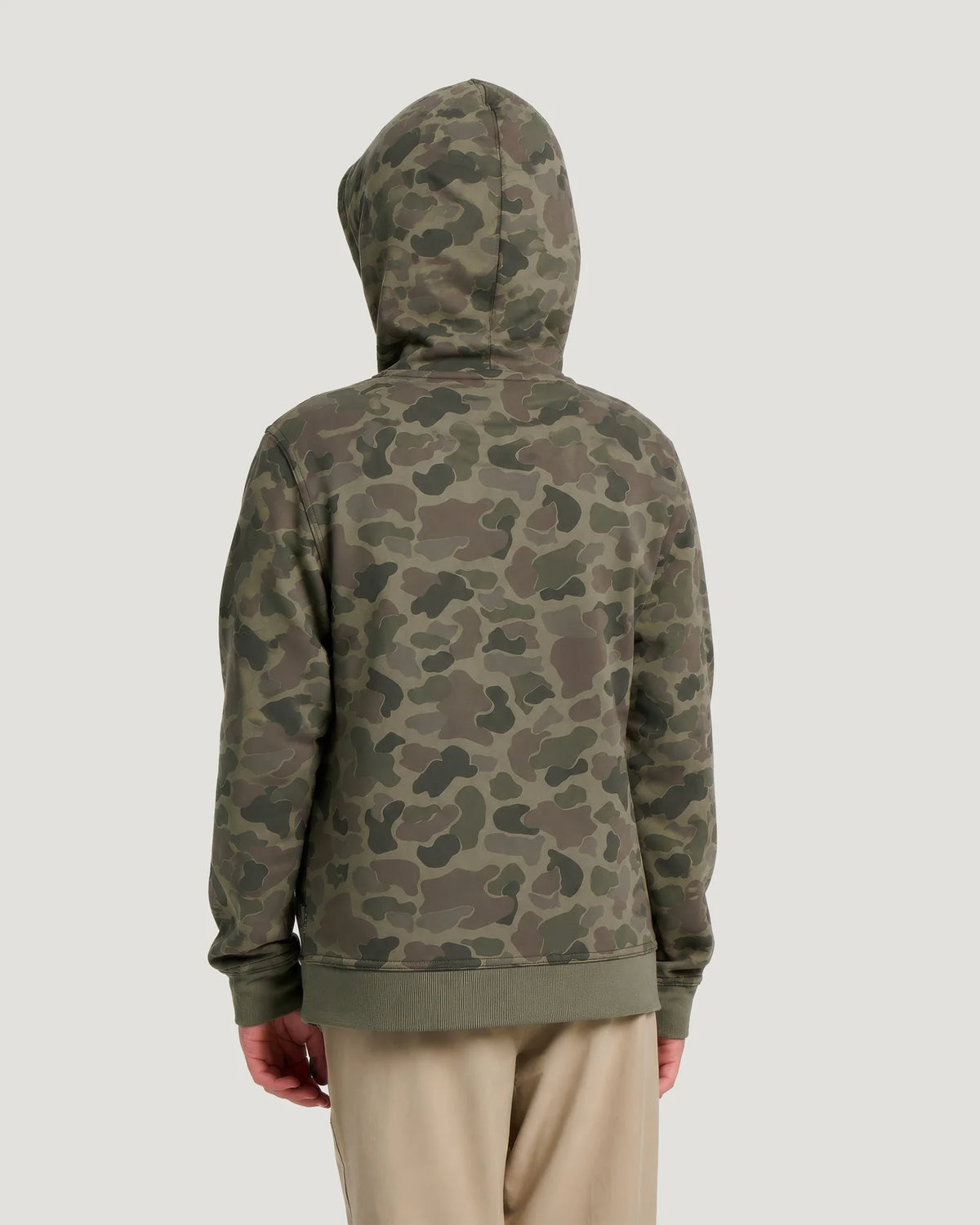 Back view of a boy wearing a camouflage hoodie and tan shorts in front of a white background. 