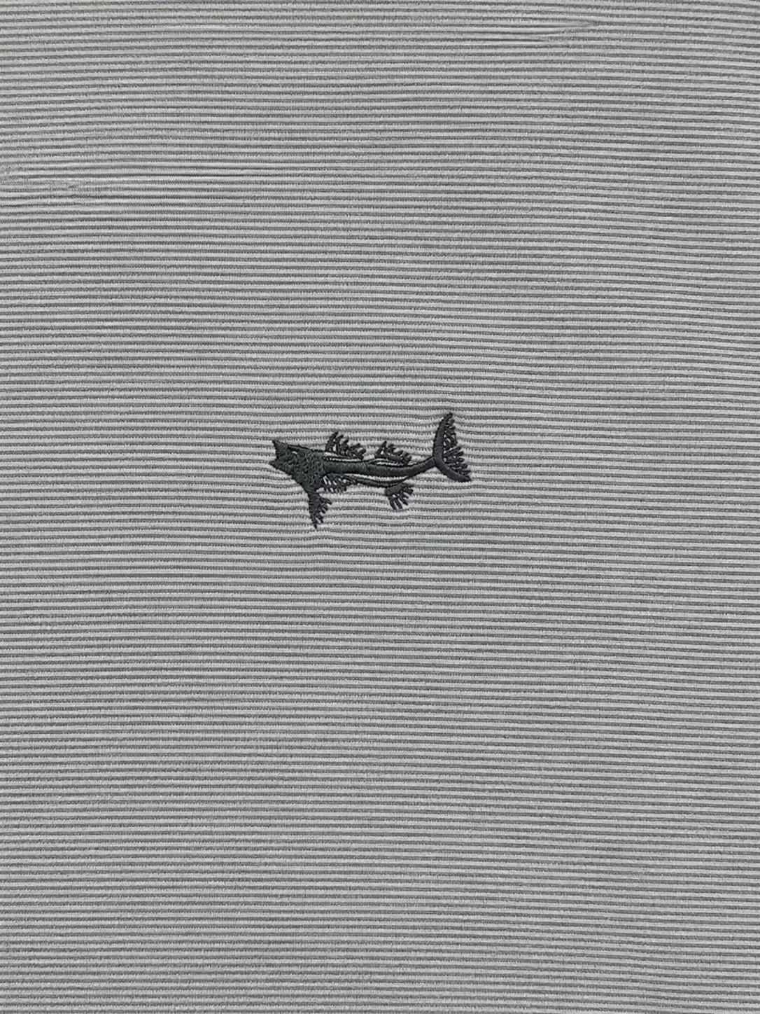 A close-up of a gray ribbed knit fabric with a small black embroidered shark logo in the center.