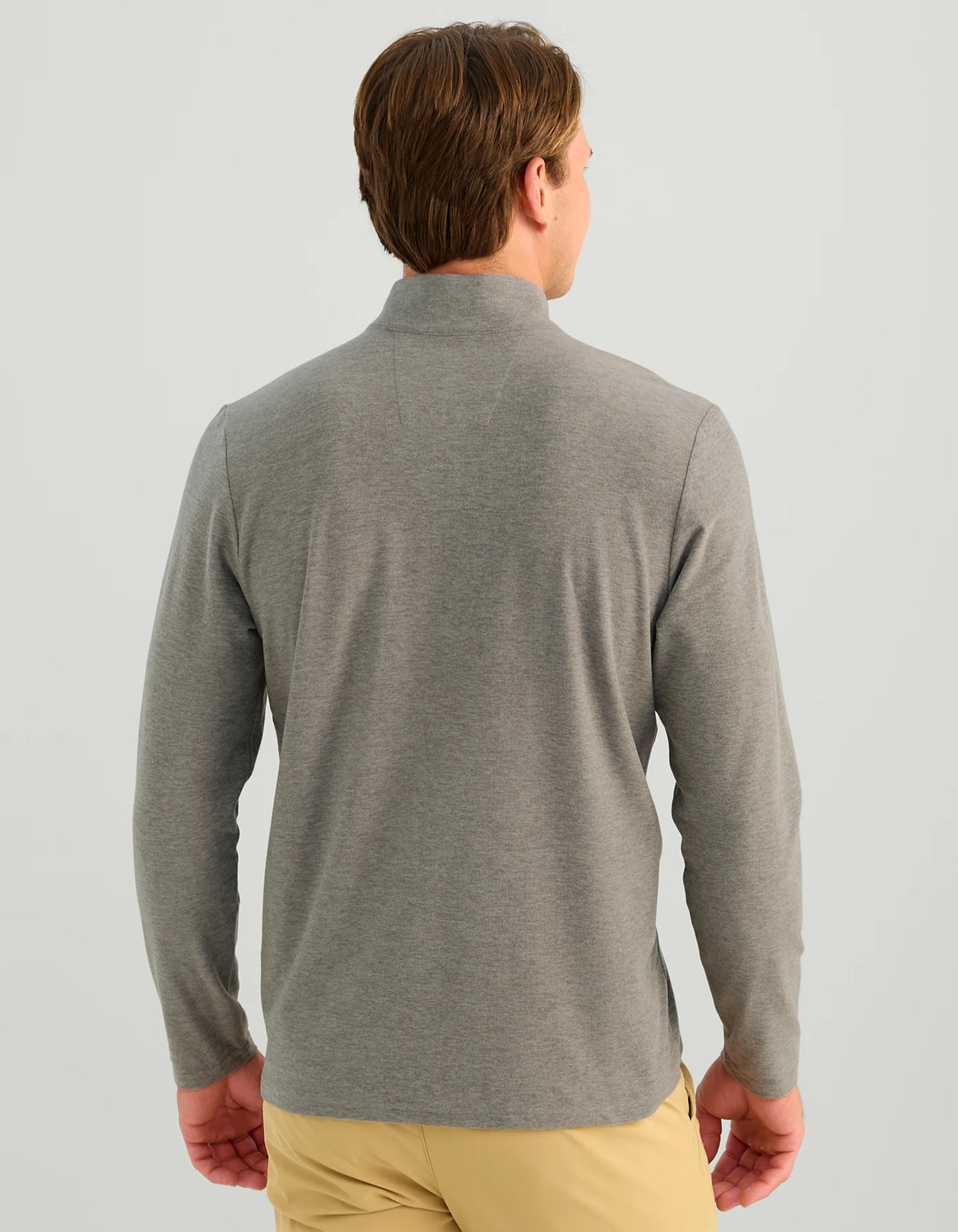 A man viewed from the back wearing a heather gray long-sleeve quarter-zip pullover and tan pants, set against a solid light gray background.