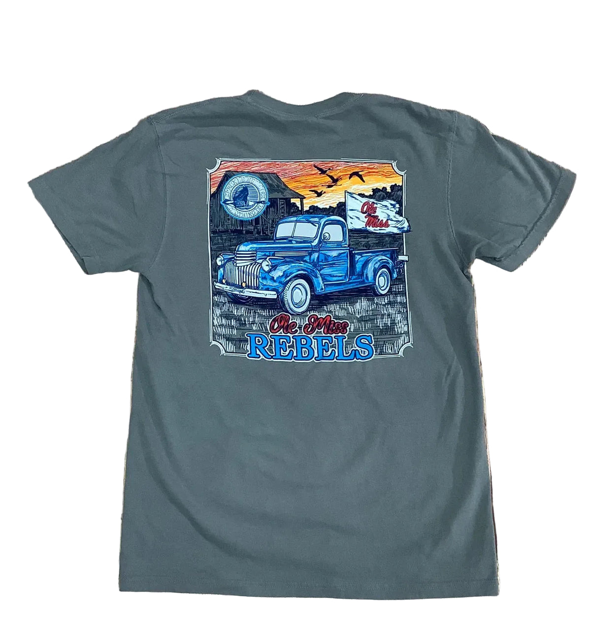 A dark gray t-shirt laid flat on a rustic wooden background, featuring a large graphic print on the back with a blue vintage pickup truck, a cowboy, a horseshoe, and the text 'The Old Rebels'.