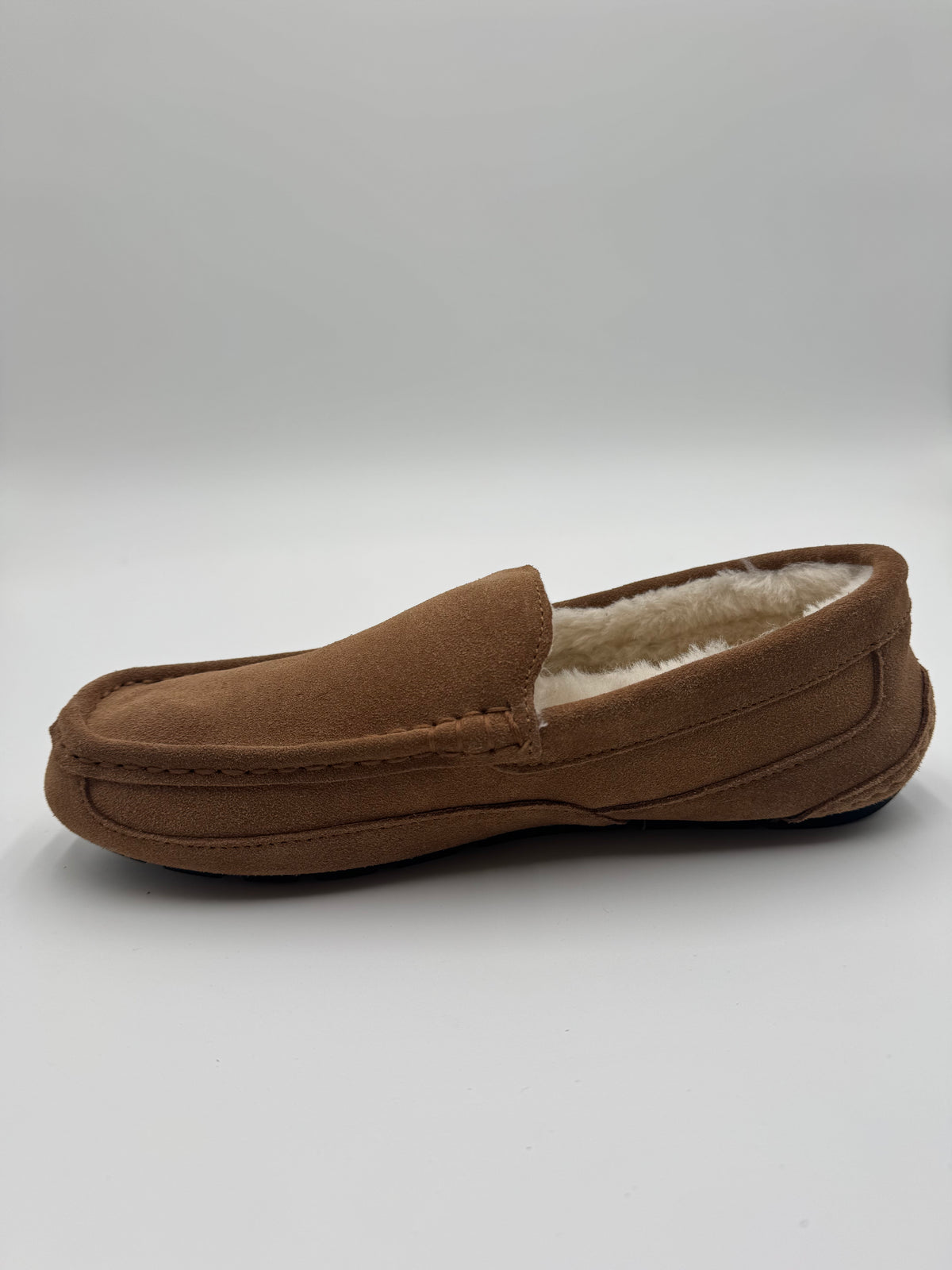 A single brown suede slip-on loafer with a soft cream-colored shearling lining, shown from a side profile view on a light gray background.