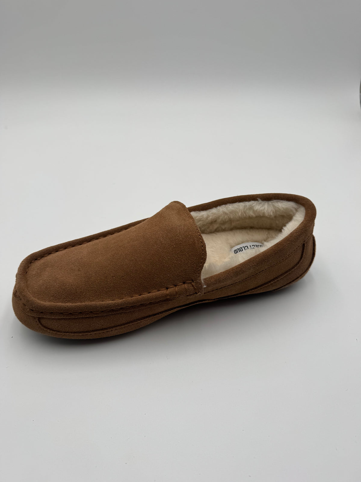 A single brown suede slipper with a cream-colored shearling lining, photographed on a light gray studio background.