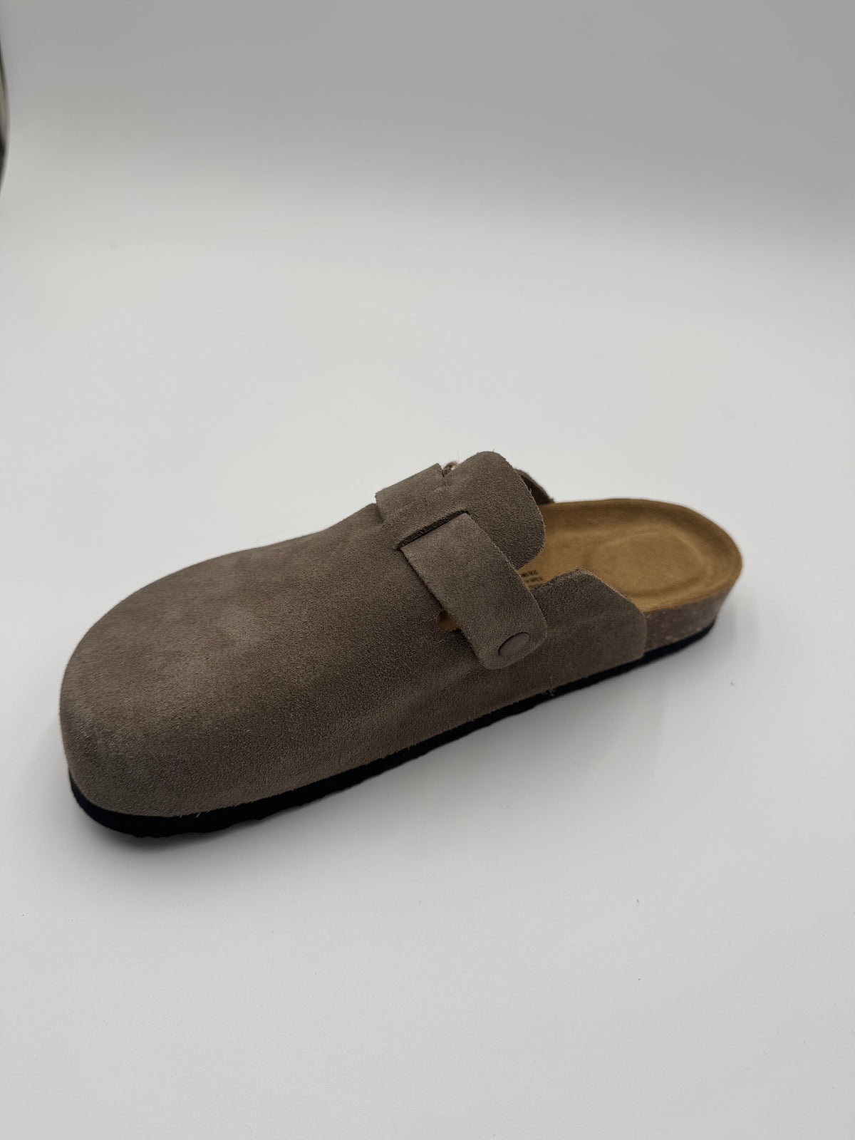 A single taupe-brown suede clog shoe with a hook-and-loop strap closure, shown from a side angle on a light gray background.