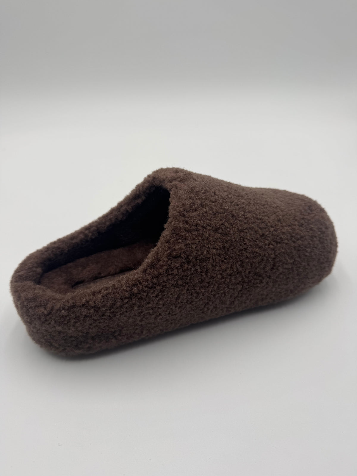 A single brown fuzzy slip-on house slipper photographed on a light gray studio background.
