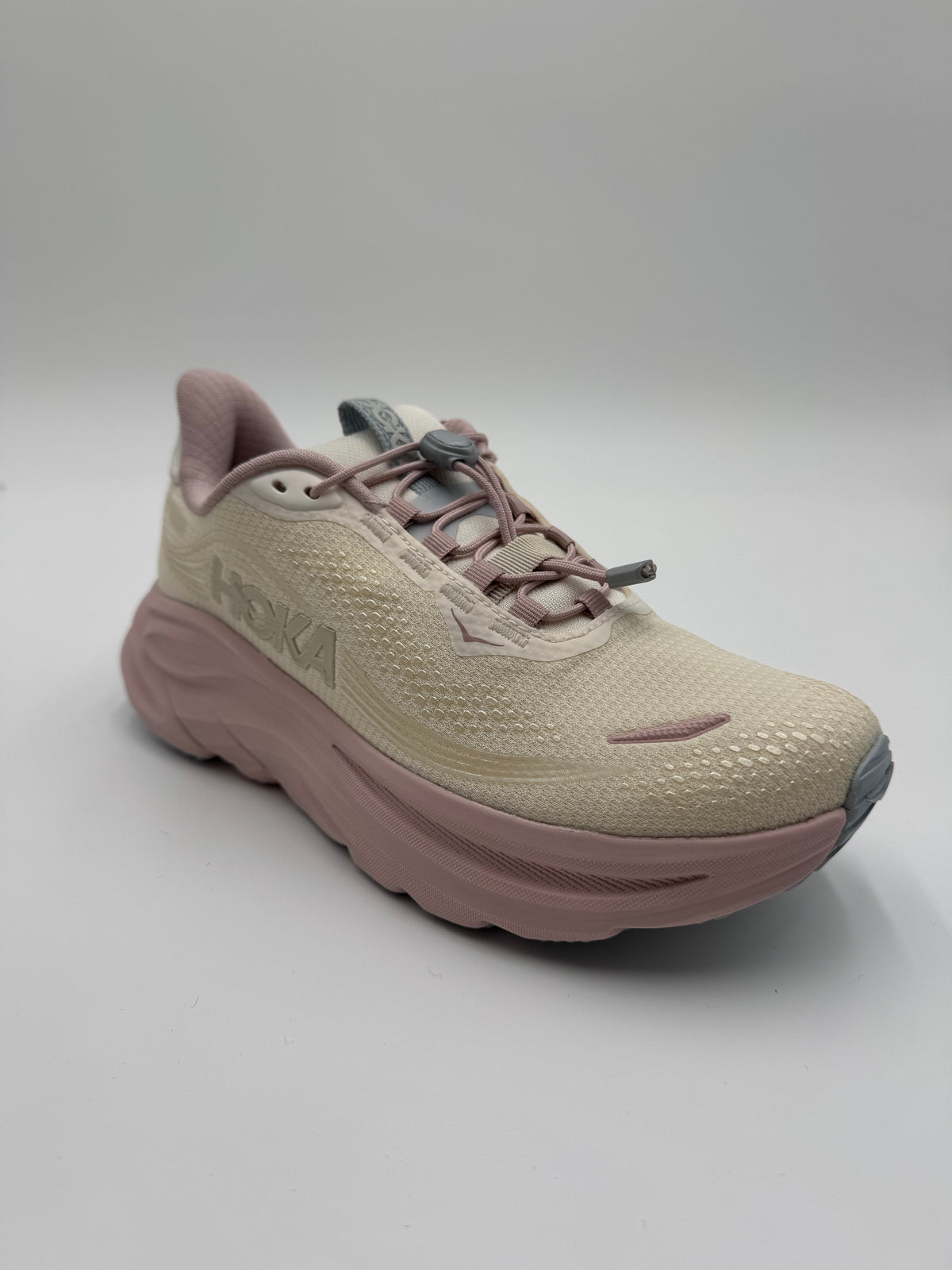 A single HOKA running shoe in beige and dusty pink, photographed from a three-quarters angle on a light gray studio background.