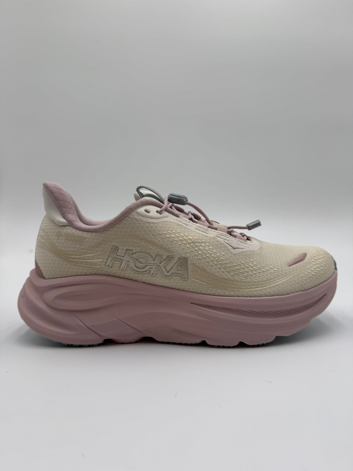 A HOKA running shoe in beige and dusty pink, shown from a side profile view against a neutral gray background.