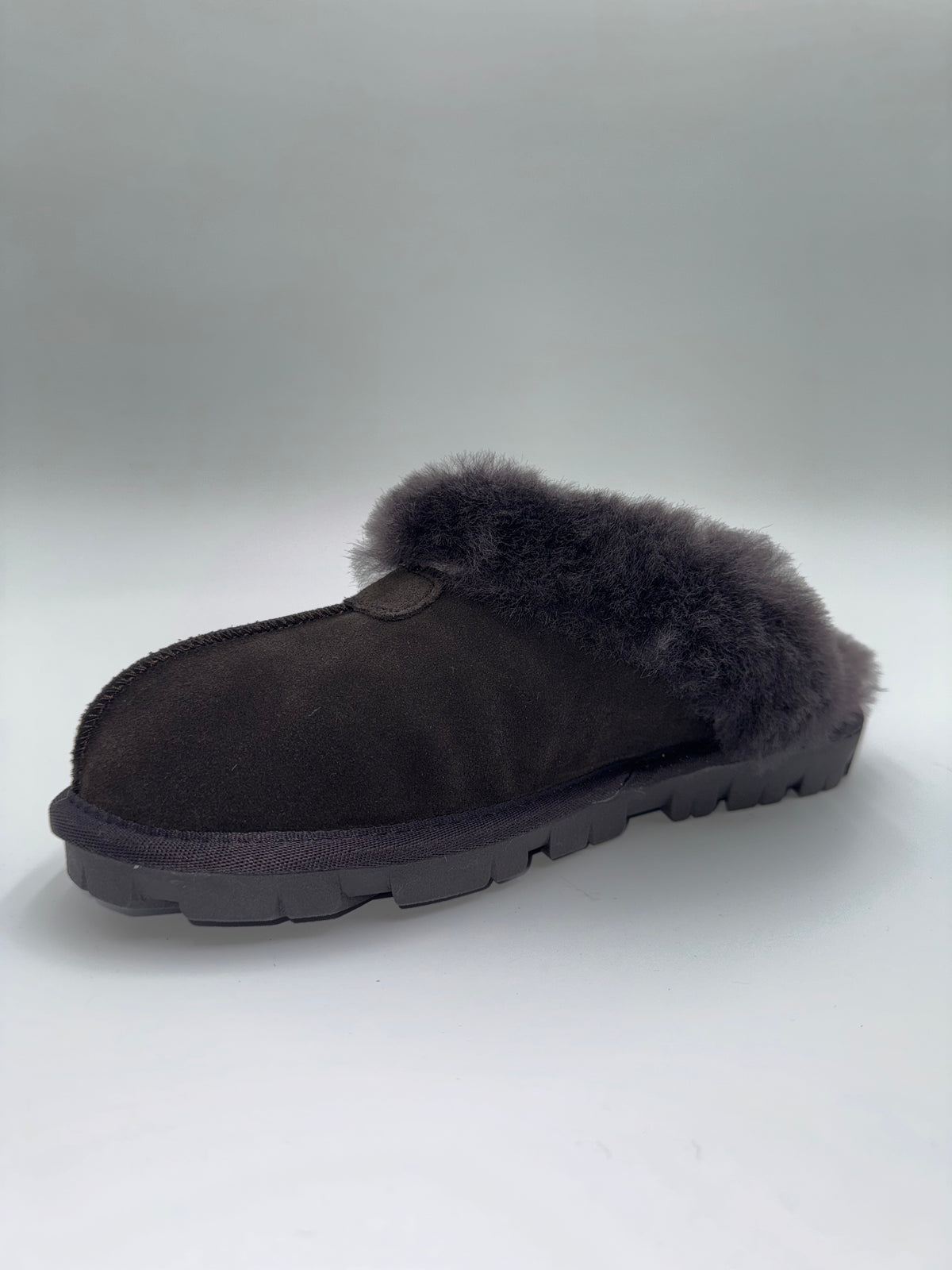 A single dark brown slip-on slipper with a thick black sole and fluffy dark brown faux-fur trim, photographed on a light gray studio background.