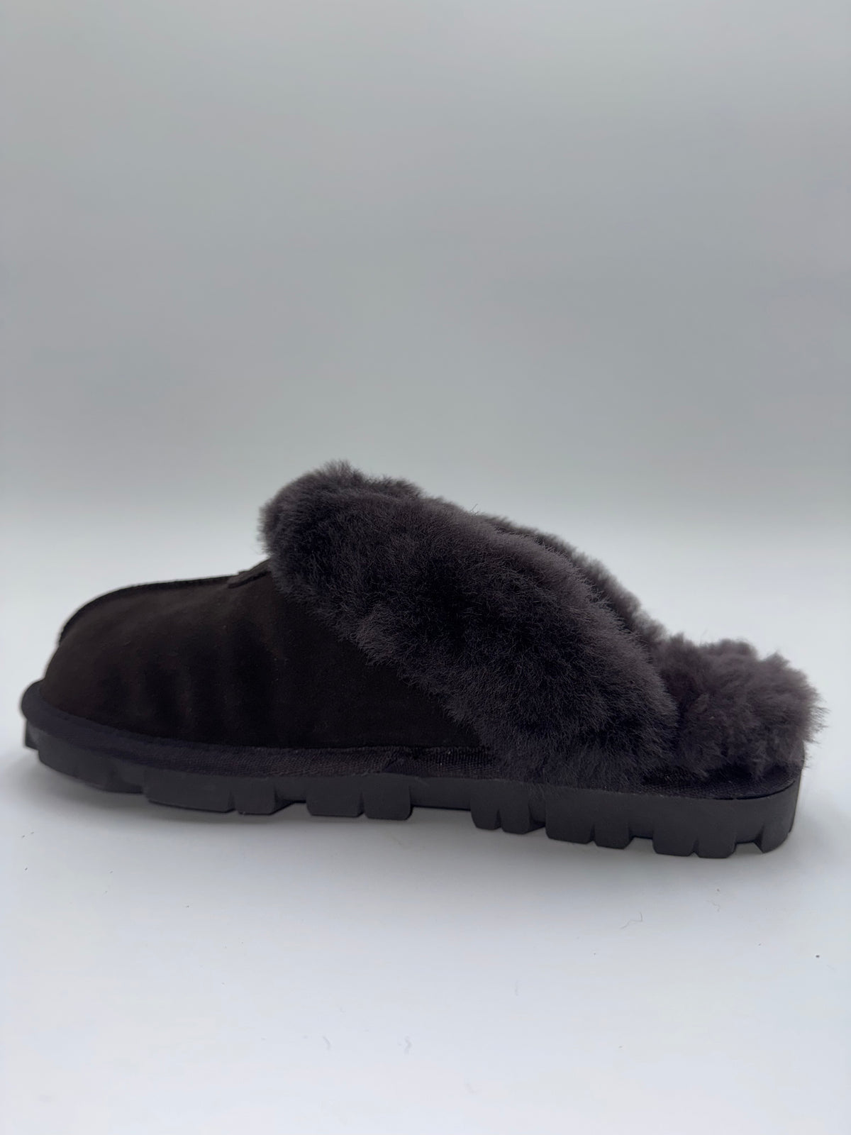A single black slip-on mule slipper with a soft black faux-fur collar and a chunky black sole, photographed against a neutral light gray background.