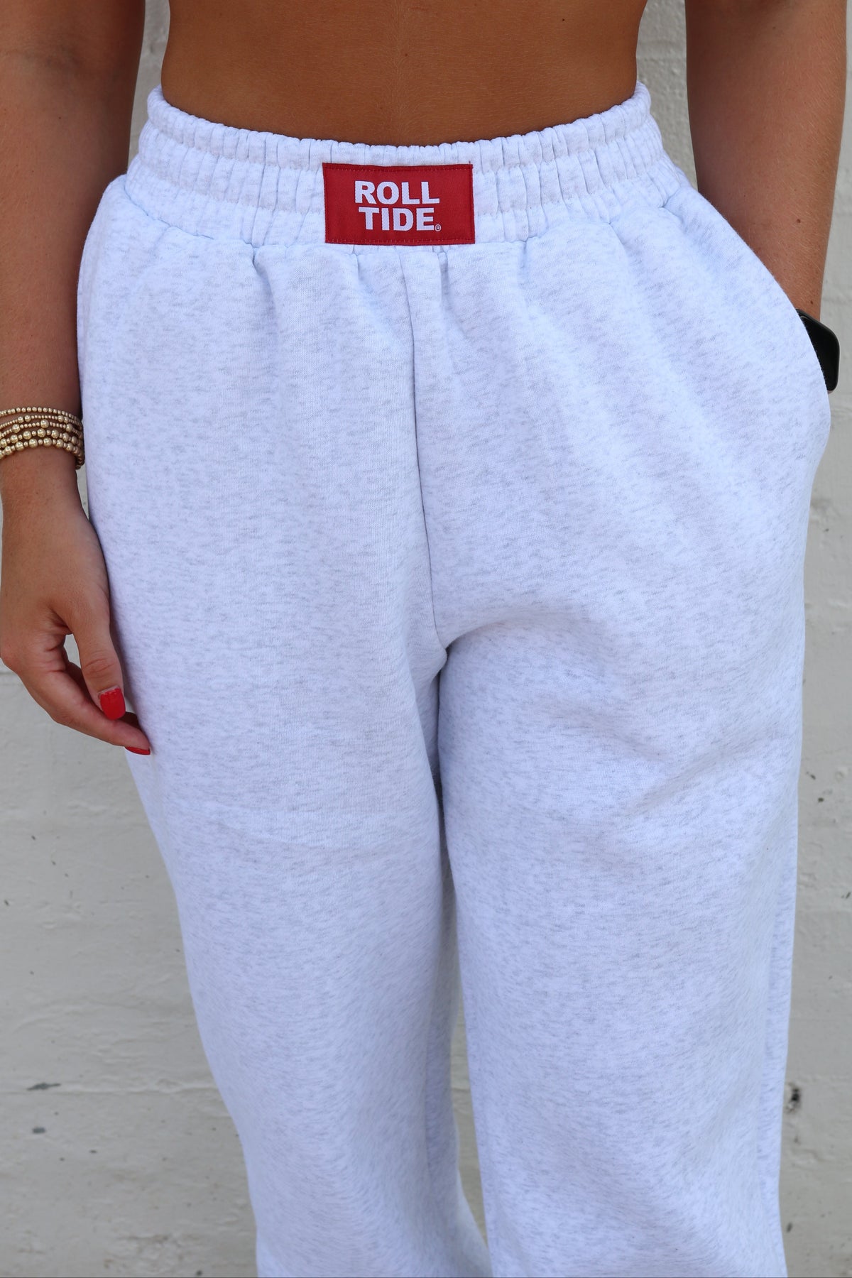 A person wearing light heather gray sweatpants with a red waistband label that reads 'ROLL TIDE'. The photo is cropped from the chest down, showing the pants against a light wall.