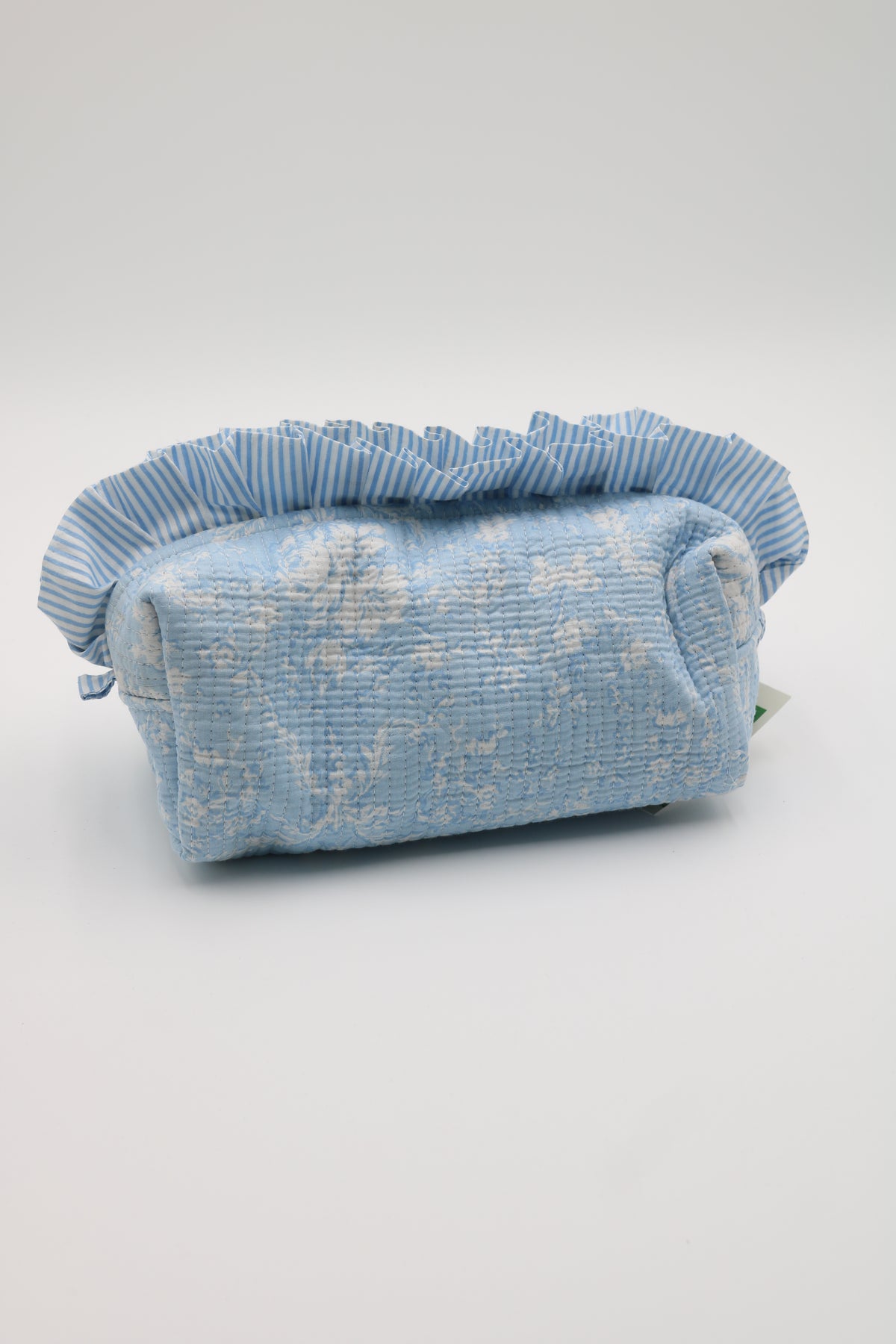 A light blue textured fabric pouch with a ruffled top trim, featuring a subtle white floral pattern, photographed on a neutral light gray background.