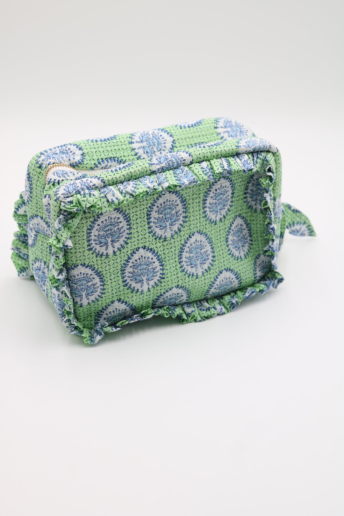 A small rectangular woven pouch or cosmetic bag with a green base, blue and white circular floral pattern, and fringed edges, photographed on a plain light background.