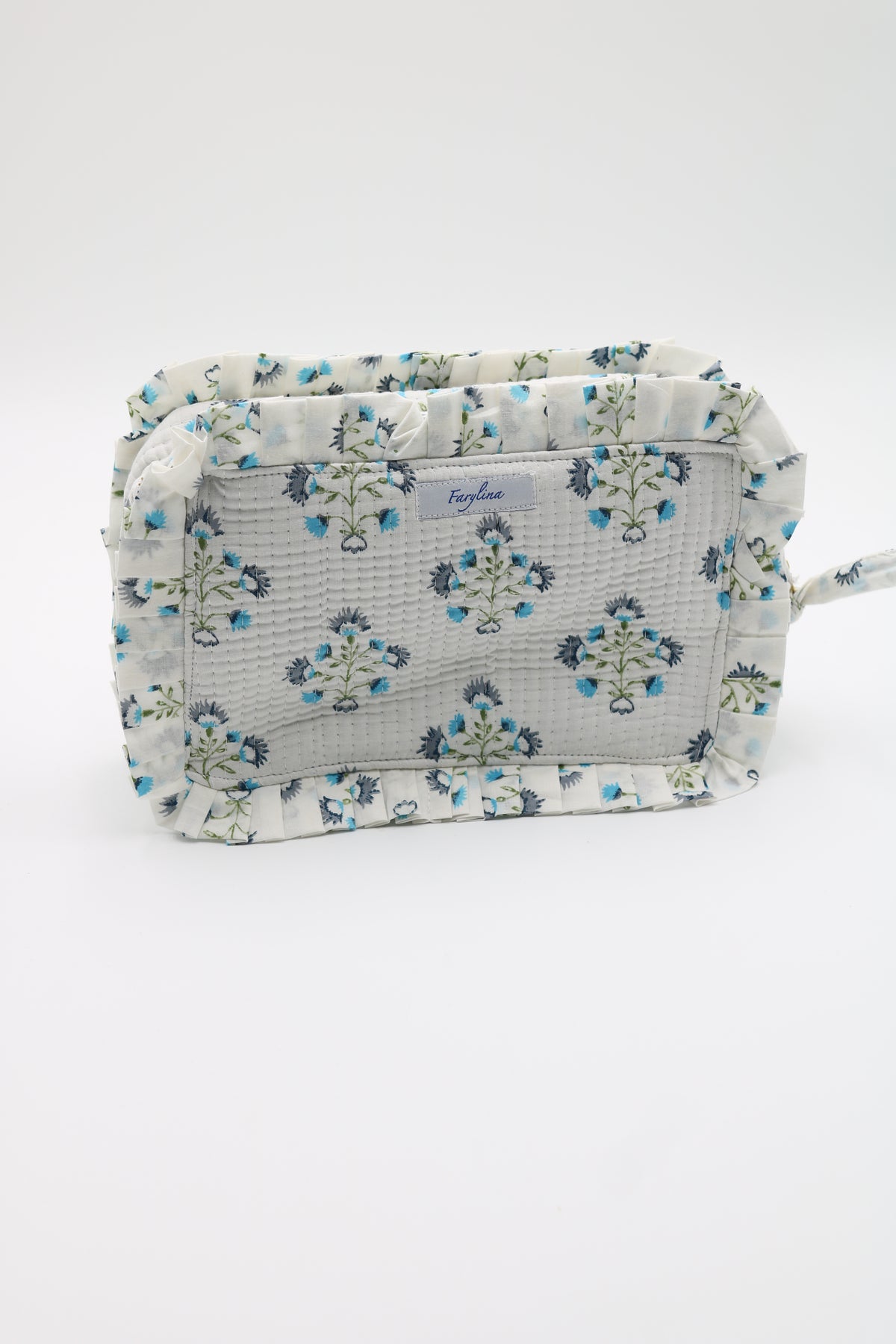 A rectangular makeup bag with a ruffled edge, featuring a light gray and white textured fabric printed with a blue and green floral pattern. A small white brand label is visible on the front.
