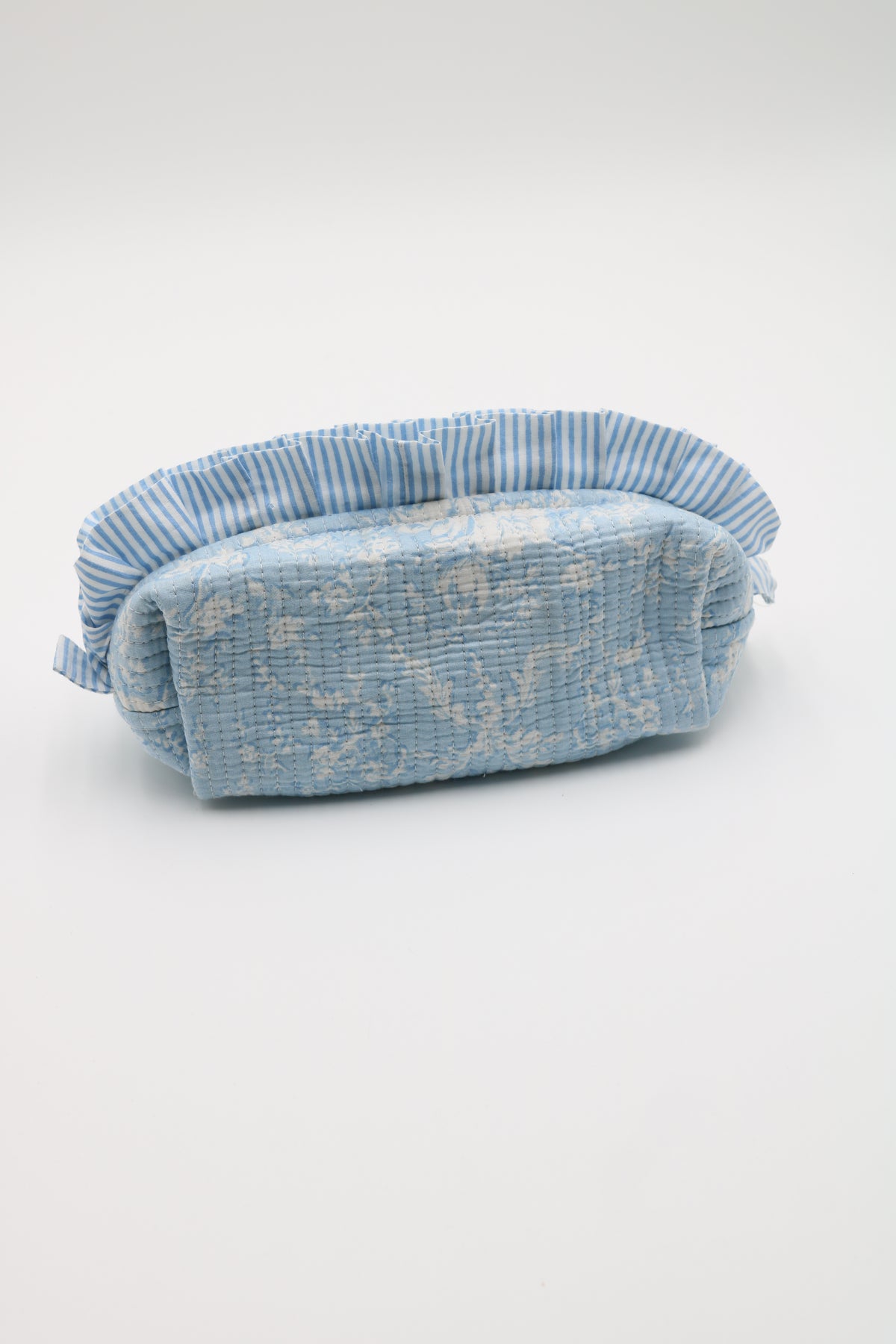 A small fabric pouch or cosmetic bag in light blue and white textured material with a striped fabric trim, photographed on a plain light gray studio background.