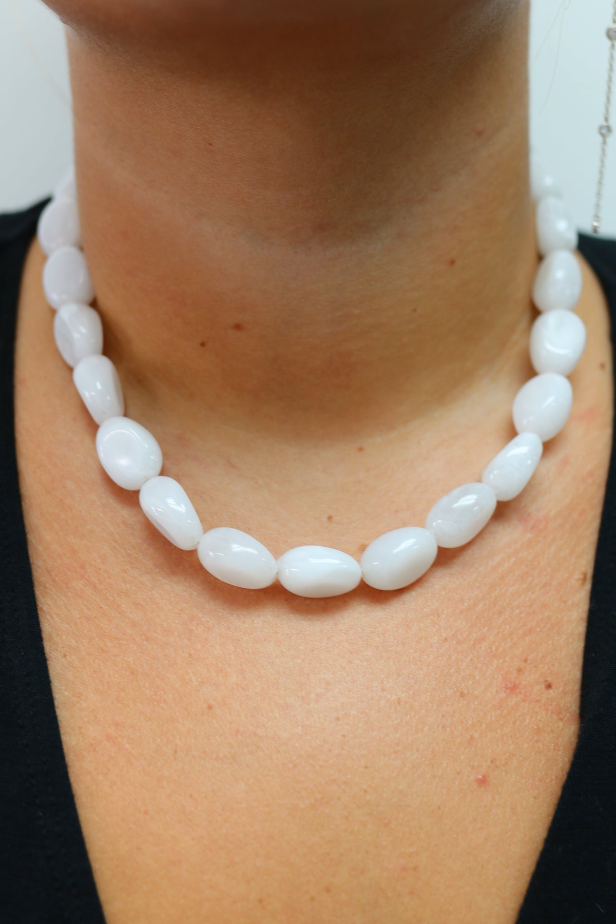 A close-up of a person wearing a double-strand white beaded necklace with smooth, rounded teardrop-shaped beads over a black top.