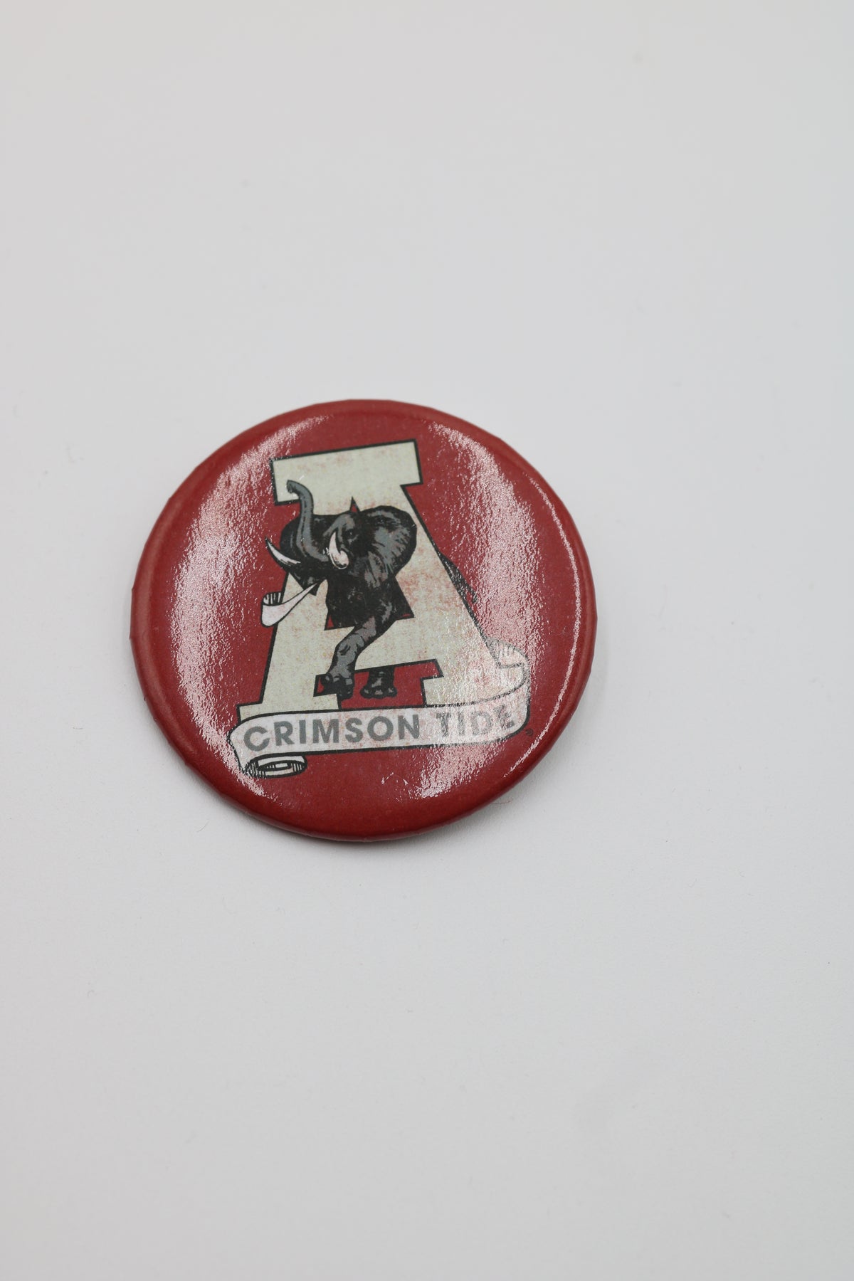 A round red button pin featuring the Alabama Crimson Tide logo with a black elephant and a large letter A on a light background.