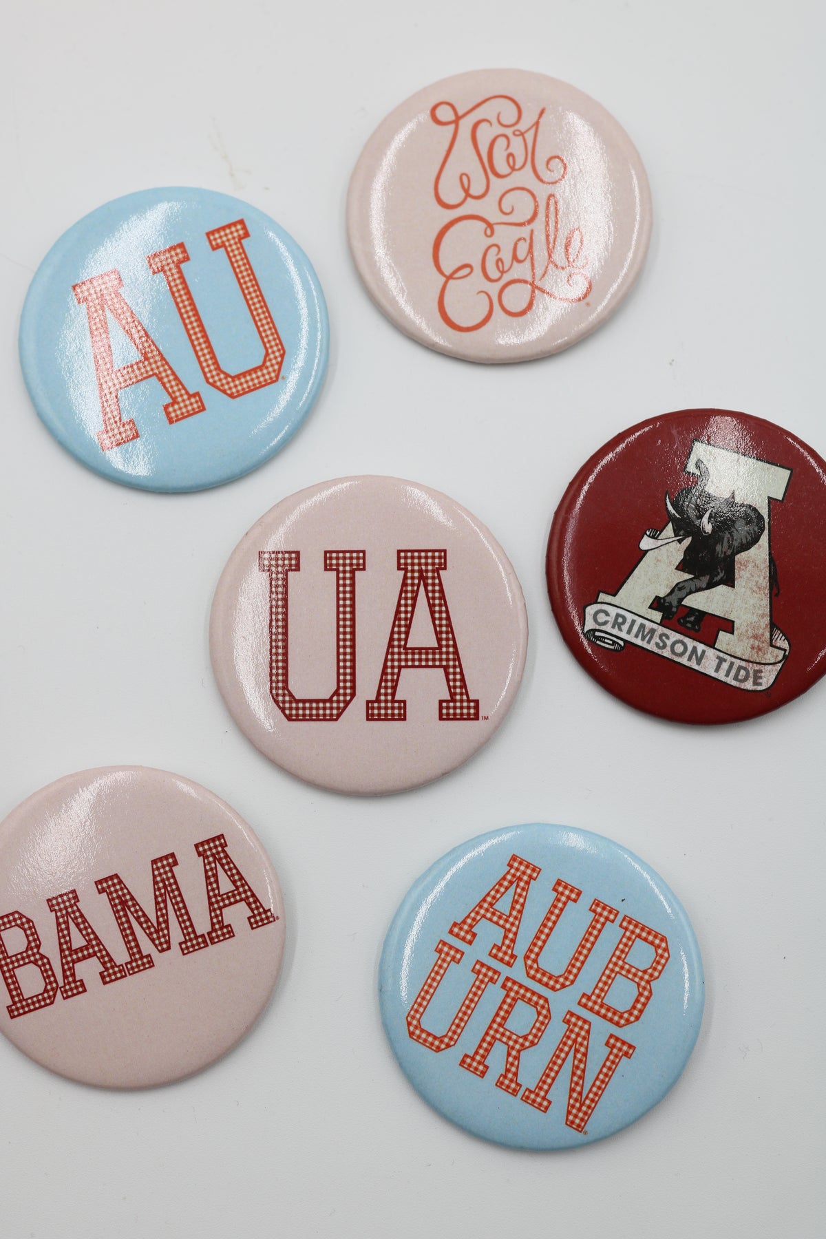 Six round button badges featuring Alabama Crimson Tide graphics and lettering, arranged on a light gray background.